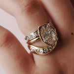A close-up of a hand wearing a gold ring with a large oval diamond center and smaller yellow gold and diamond bands.