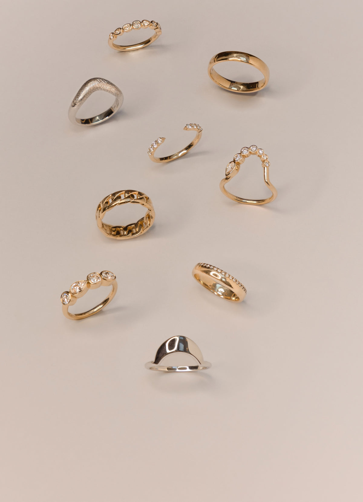 Marrow Fine stacking rings in 14k gold and white gold, including bezel-set diamond bands, a chain-link band, a curved V band and a silver signet, scattered on a soft stone background
