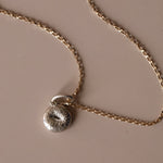 Silver Bagel Charm with yellow gold chain against a neutral background