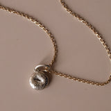 Silver Bagel Charm with yellow gold chain against a neutral background