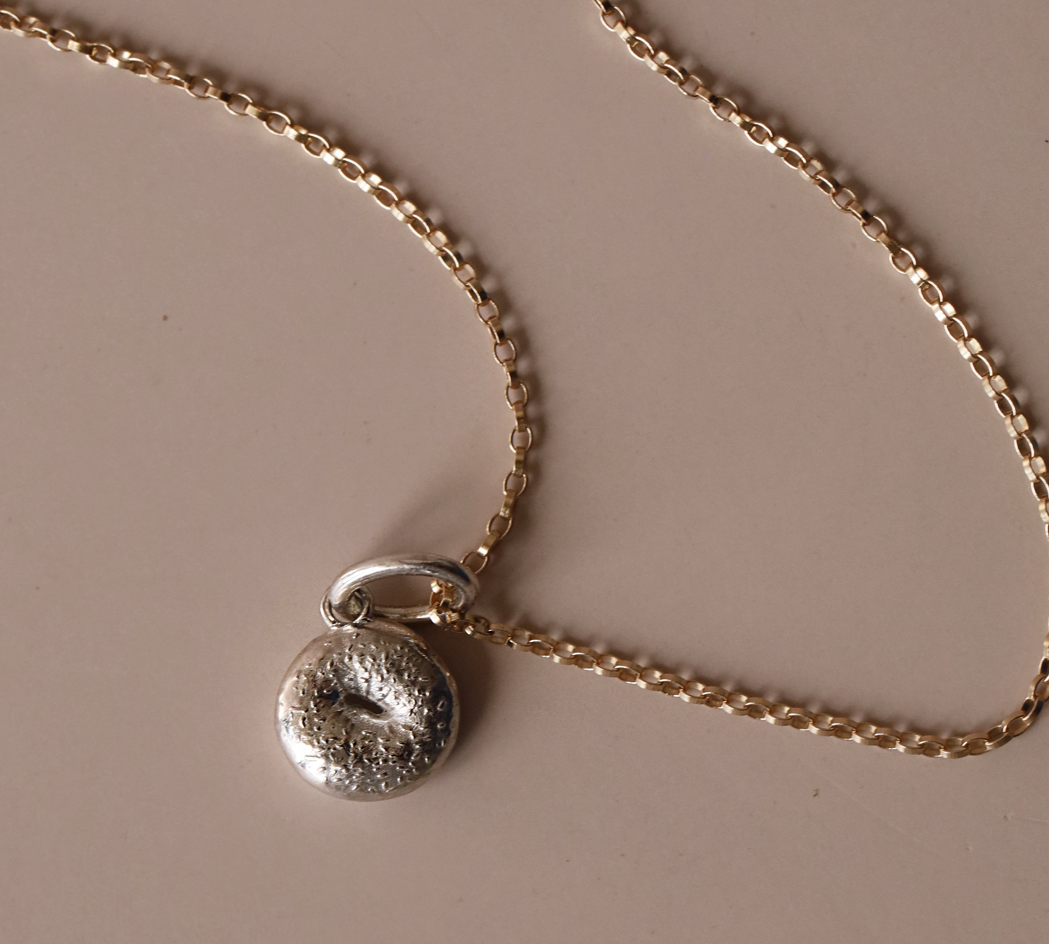 Silver Bagel Charm with yellow gold chain against a neutral background