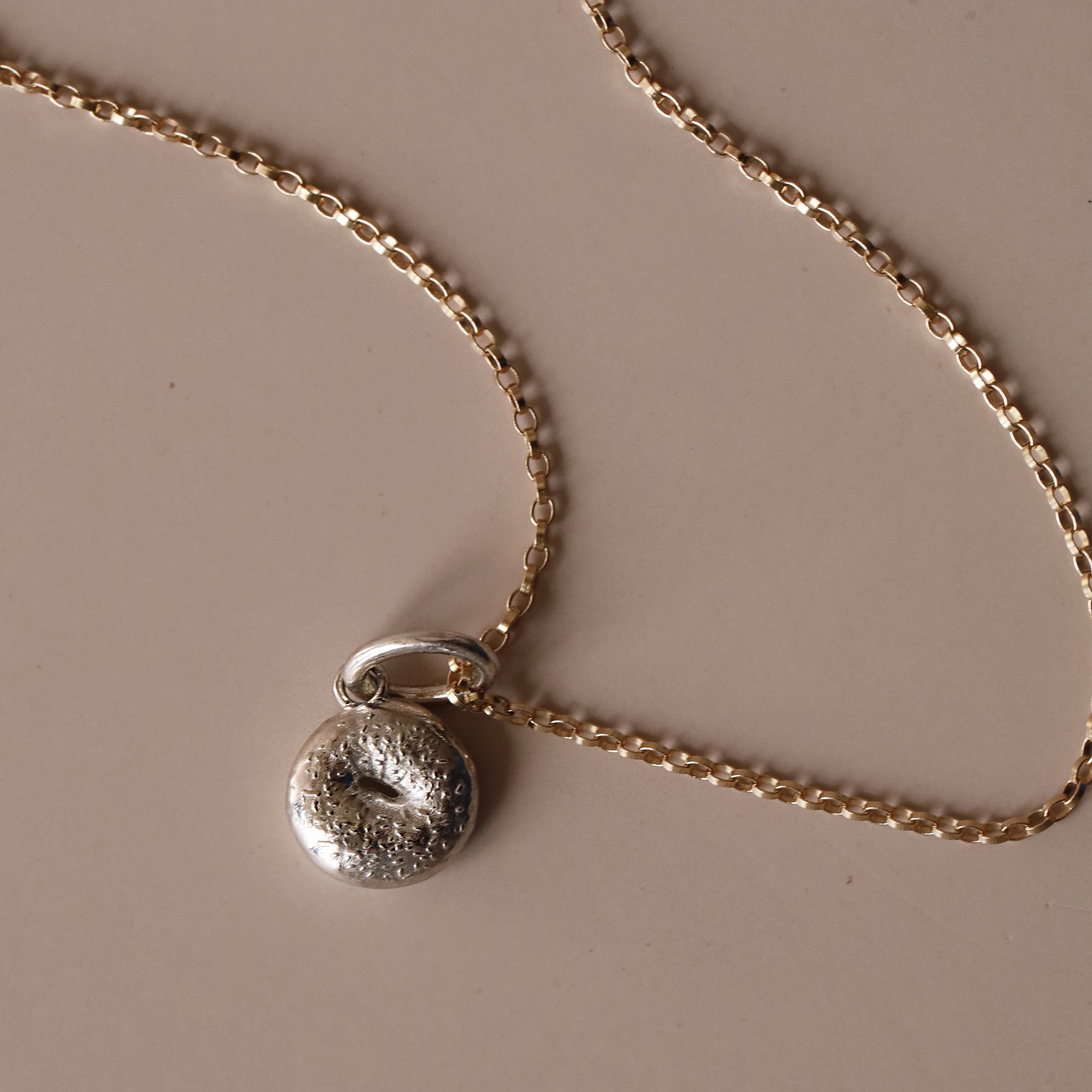 Silver Bagel Charm with yellow gold chain against a neutral background