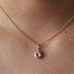 Silver Bagel Charm on yellow gold dainty chain hanging from woman's neck