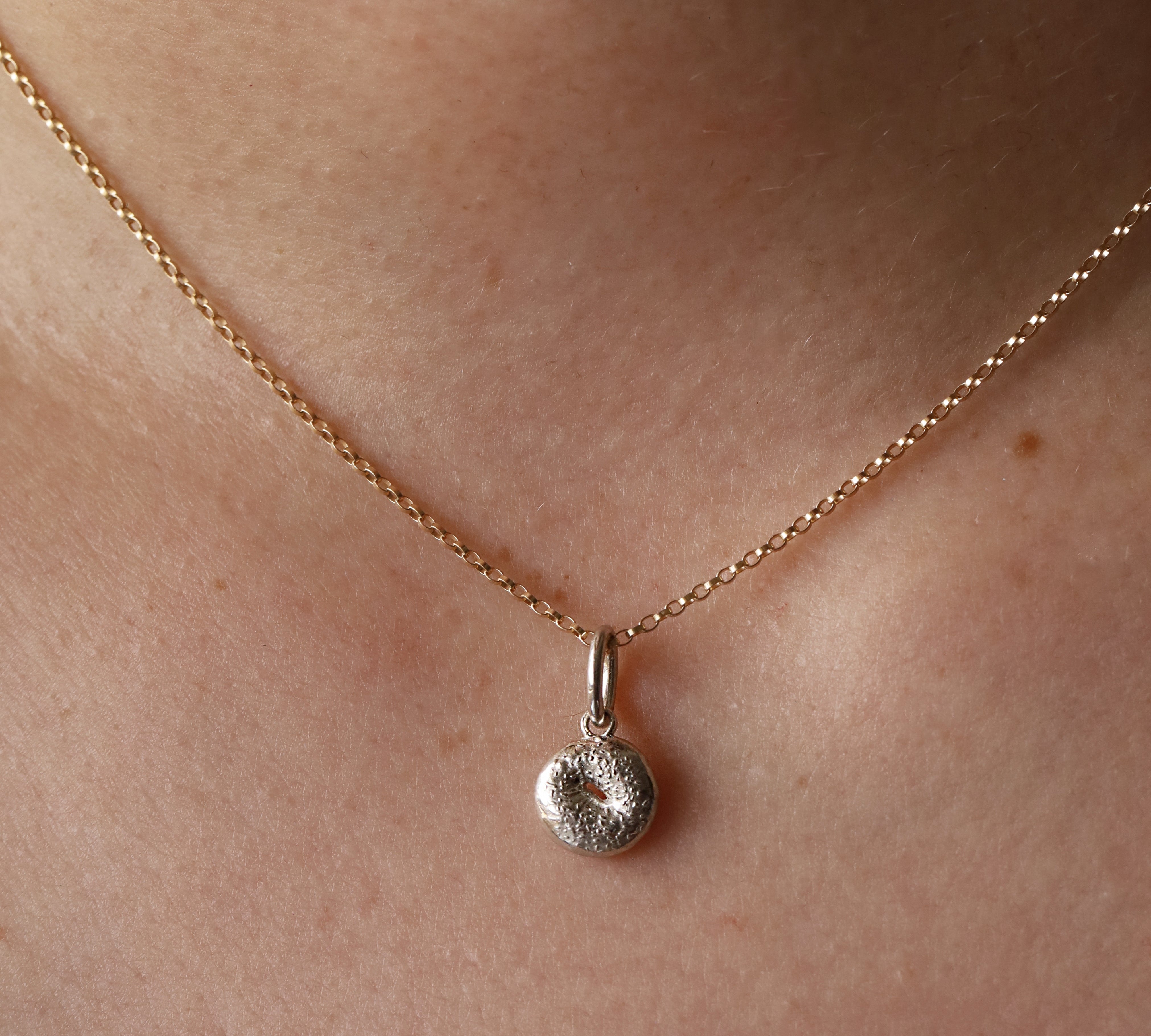 Silver Bagel Charm on yellow gold dainty chain hanging from woman's neck