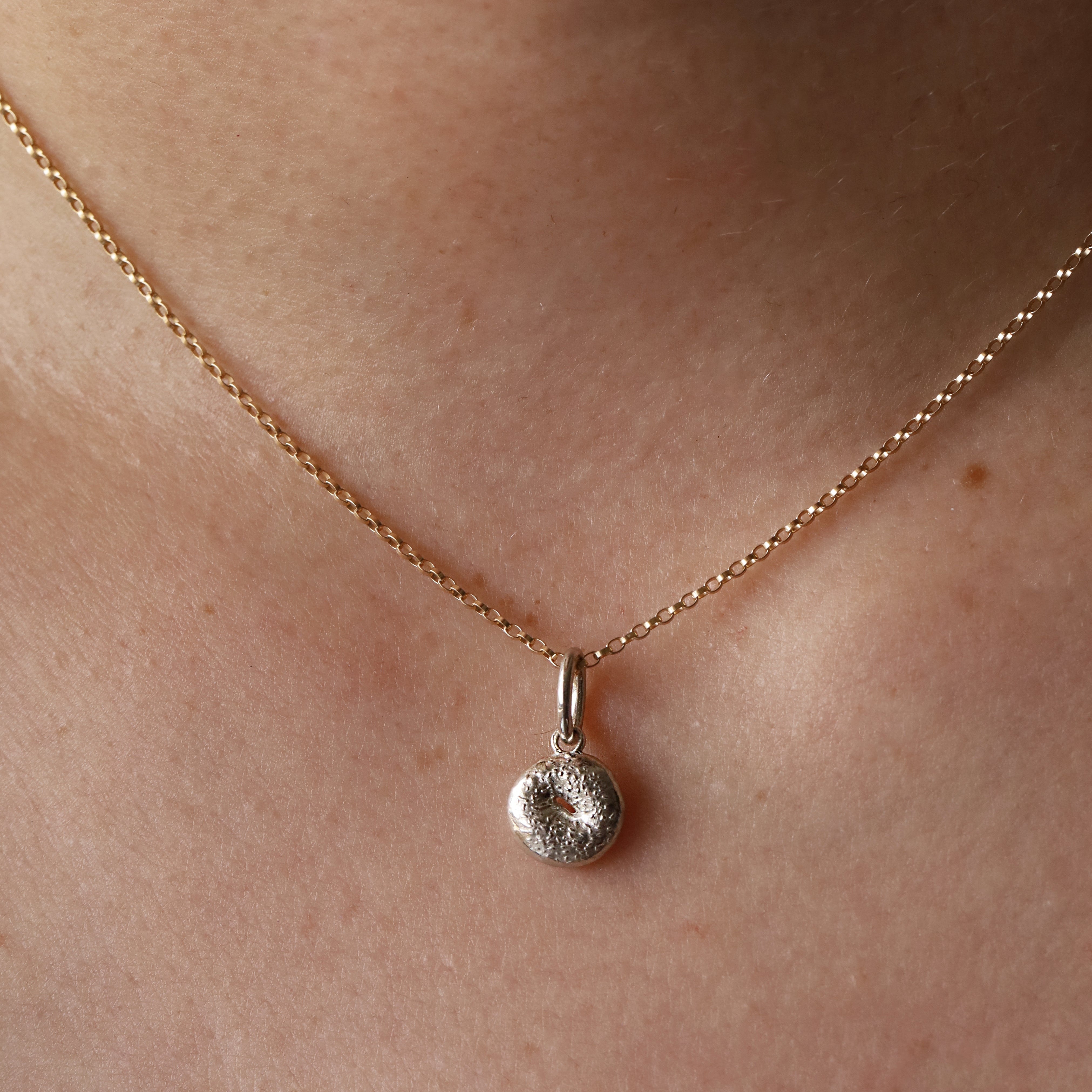 Silver Bagel Charm on yellow gold dainty chain hanging from woman's neck