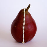 diamond tennis bracelet draped over a pear on a light background