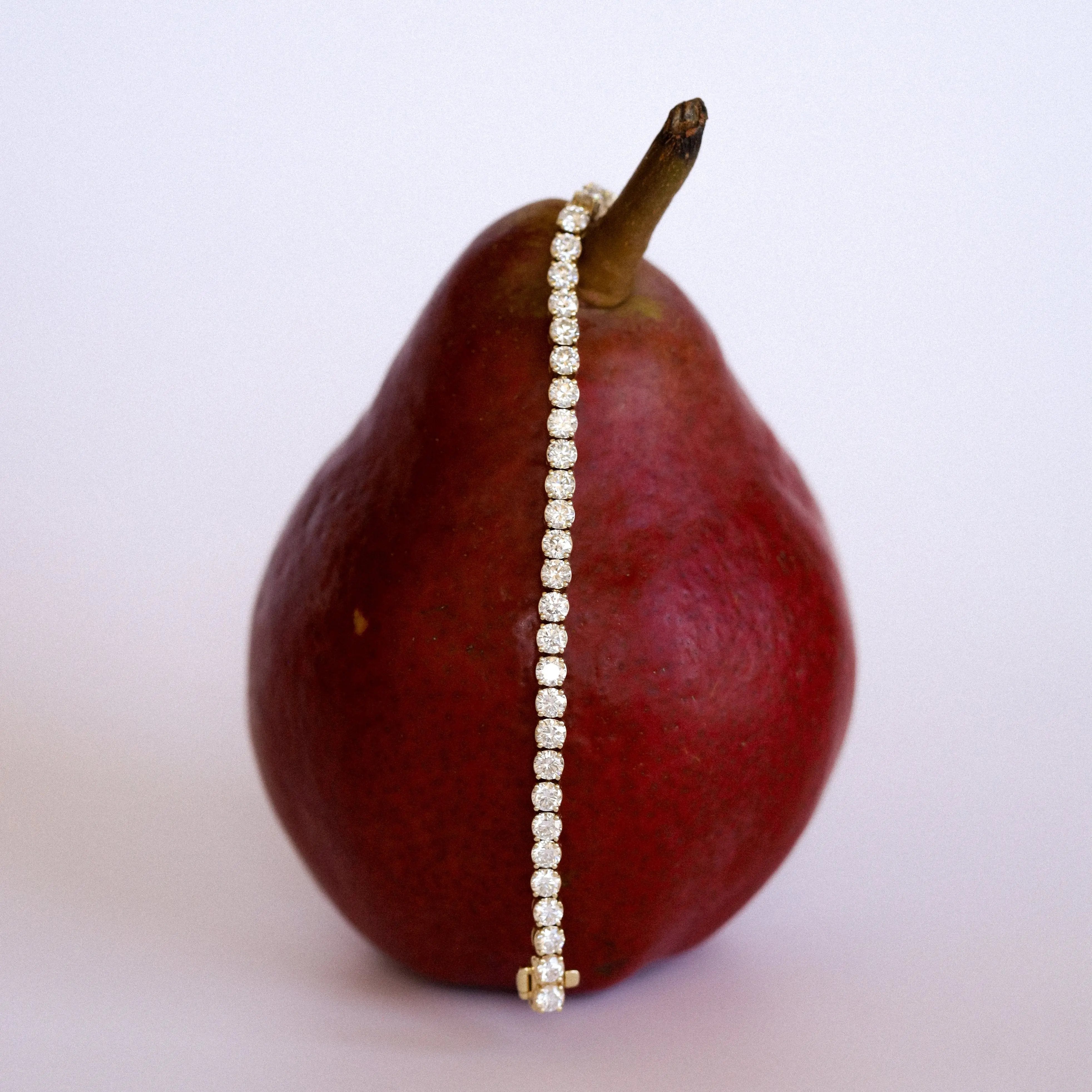 diamond tennis bracelet draped over a pear on a light background
