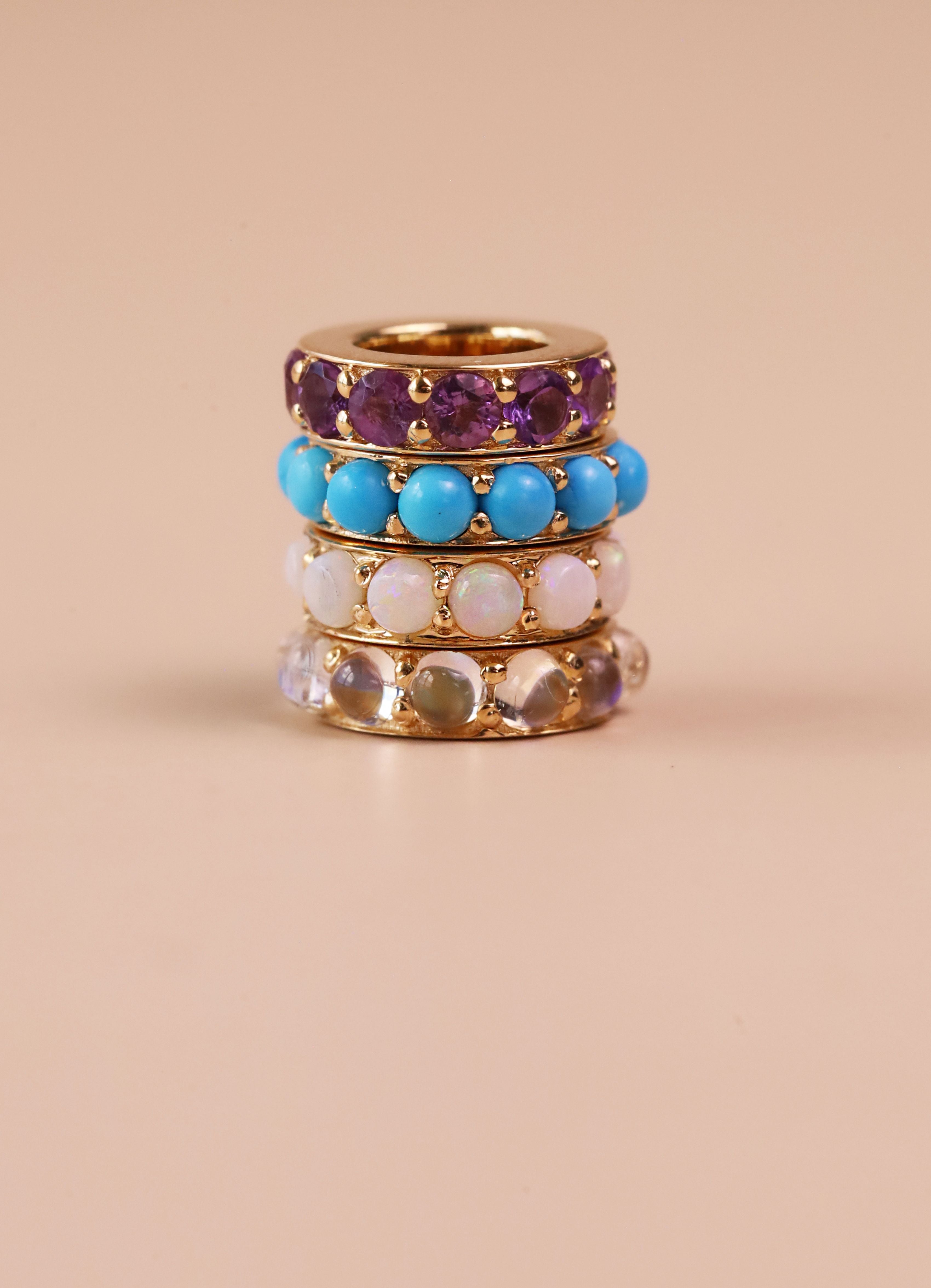stack of 4 rondelles in yellow gold featuring different colored gemstones on a neutrla/pink background