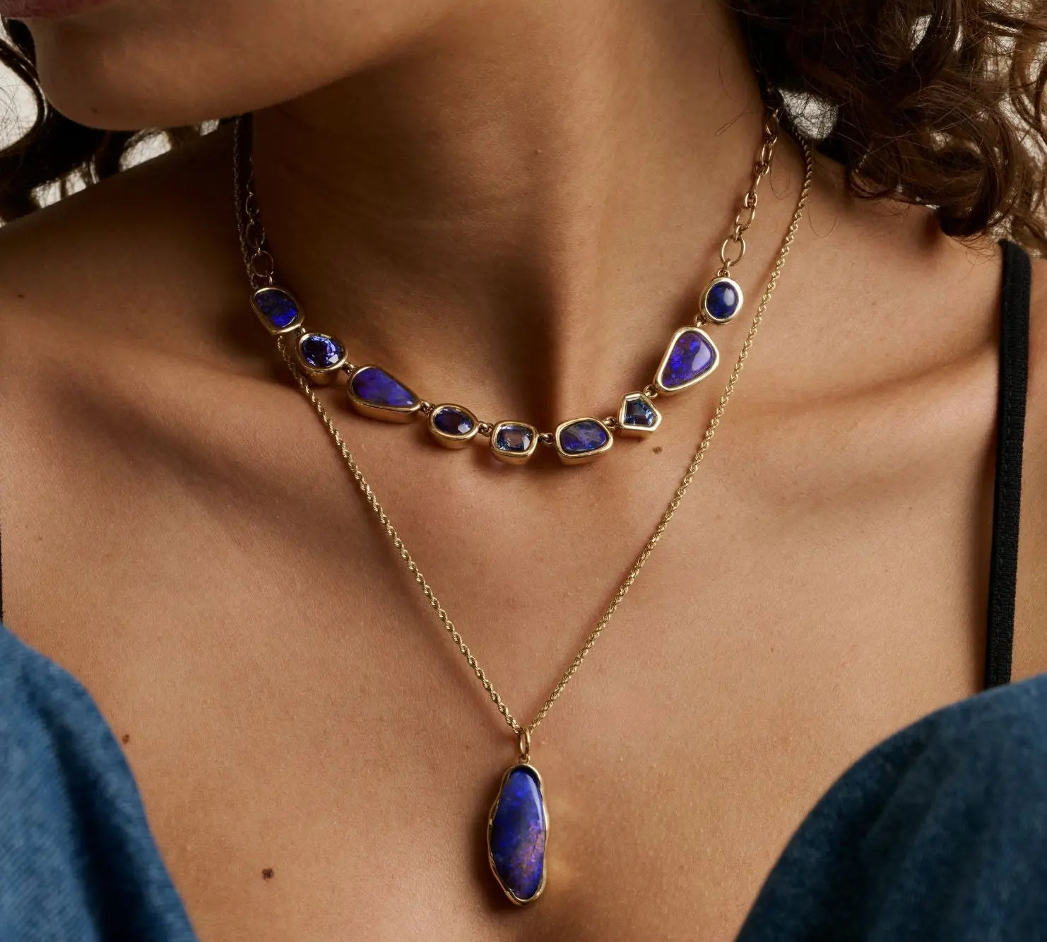 close up of woman's décolletage showcasing two statement blue gemstone necklaces layered together