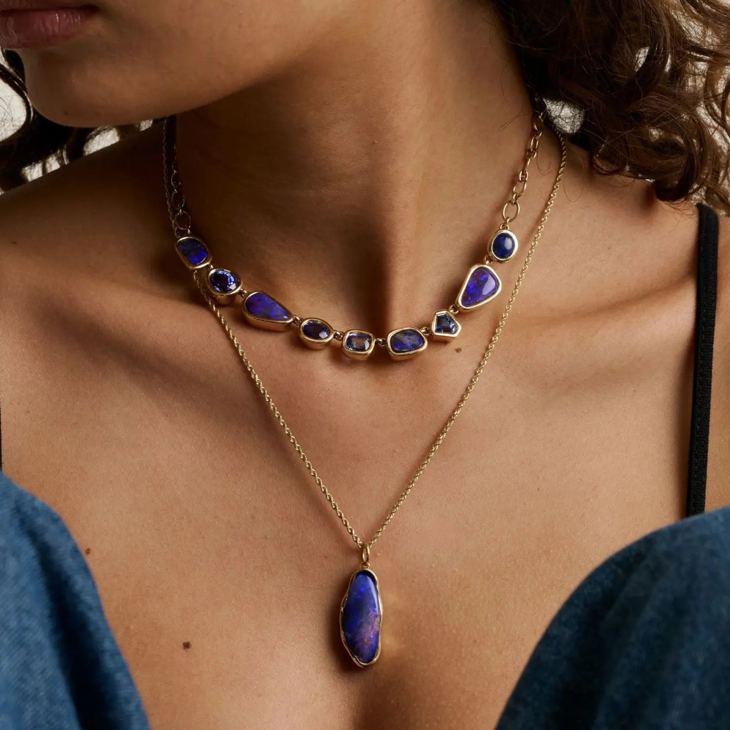 close up of woman's décolletage showcasing two statement blue gemstone necklaces layered together