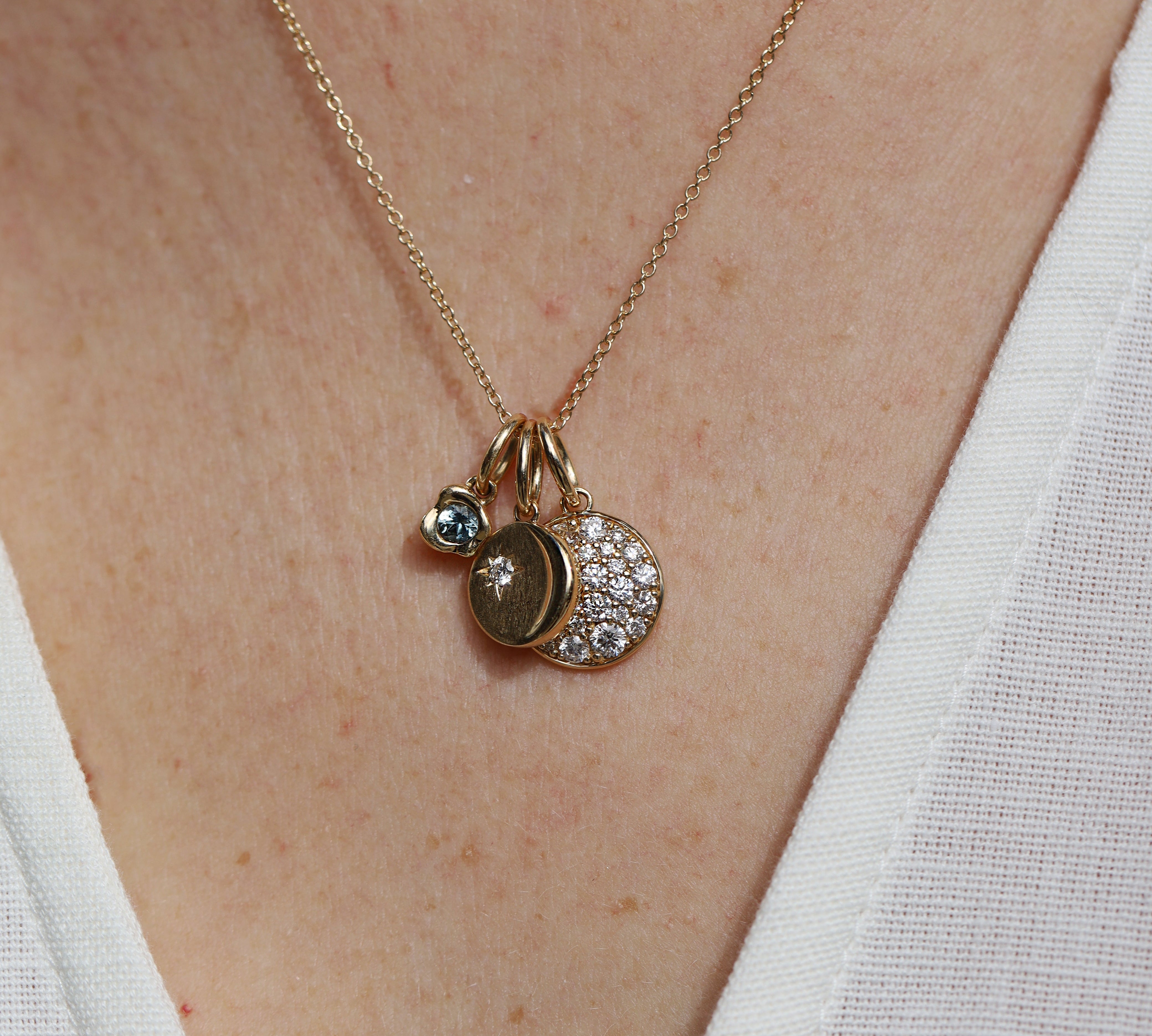 Necklace with three charms on a person wearing a white top