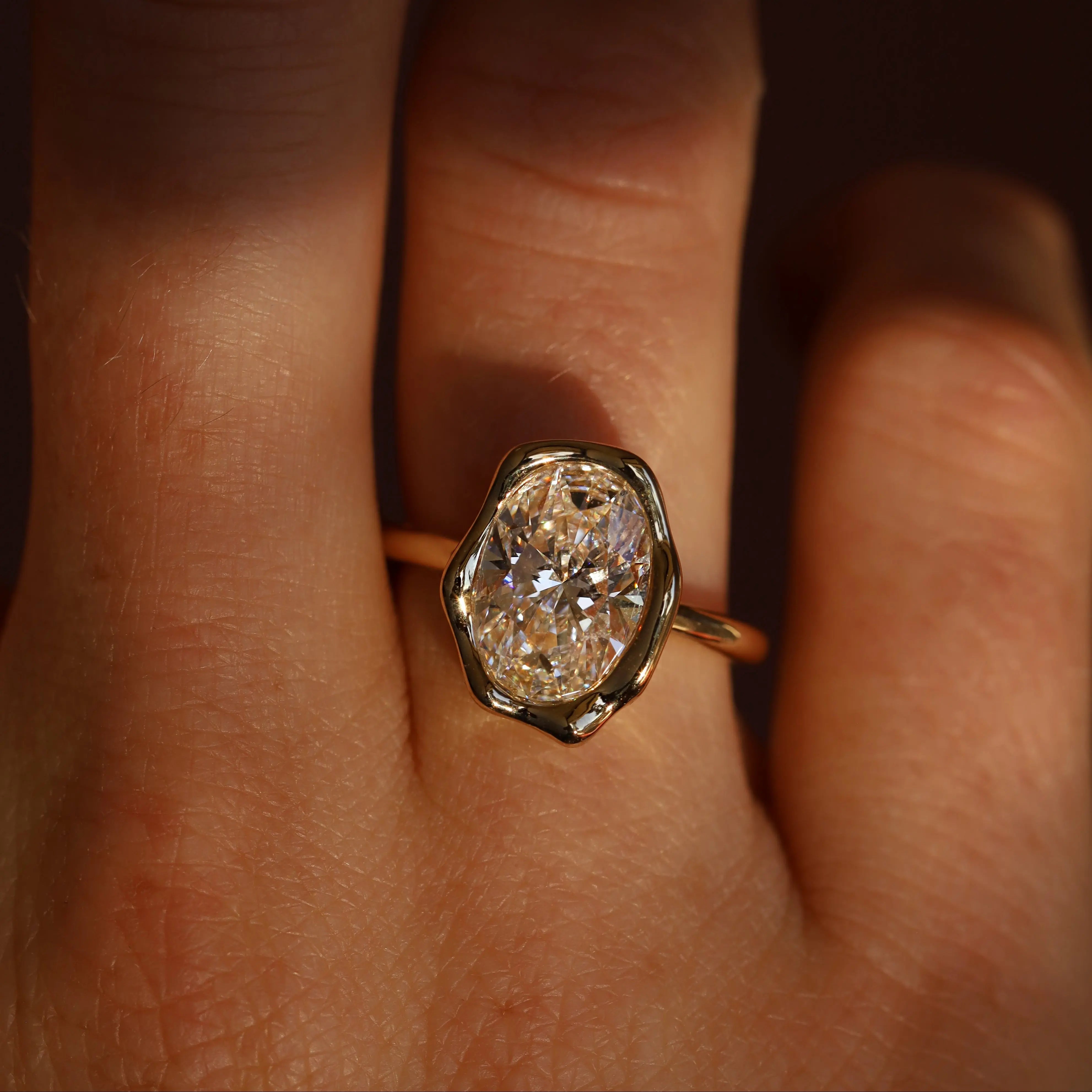 The Abstract Bezel Oval Engagement Ring worn on the finger