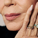 Close-up of a woman's face with a hand gently touching her cheek, wearing multiple rings.