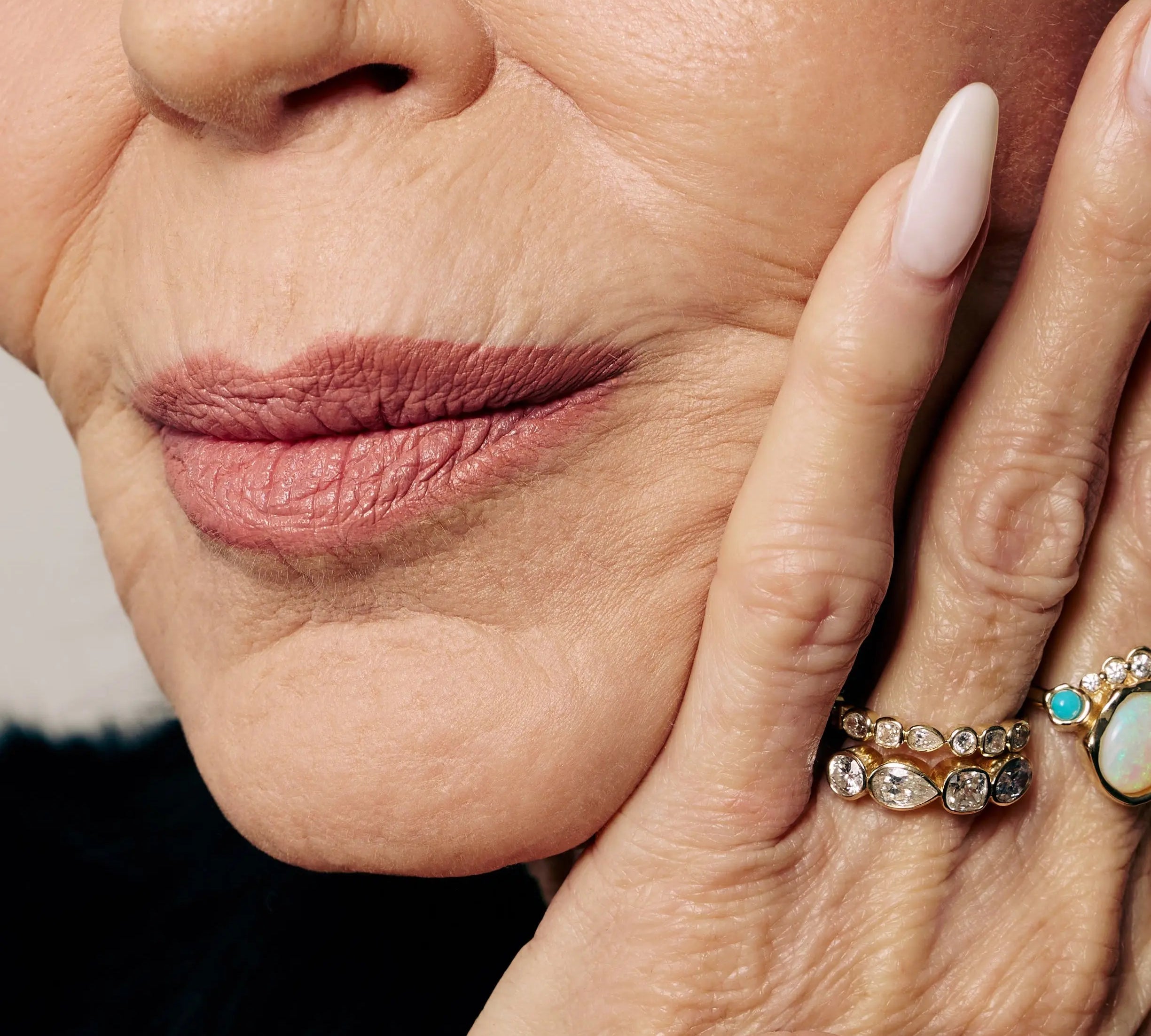 Close-up of a woman's face with a hand gently touching her cheek, wearing multiple rings.