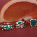 Three gold rings with emerald and diamond stones on a red background