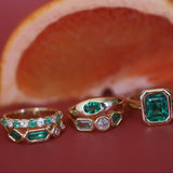 Three gold rings with emerald and diamond stones on a red background