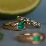 Gold ring with emerald and diamond accents on a reflective surface.