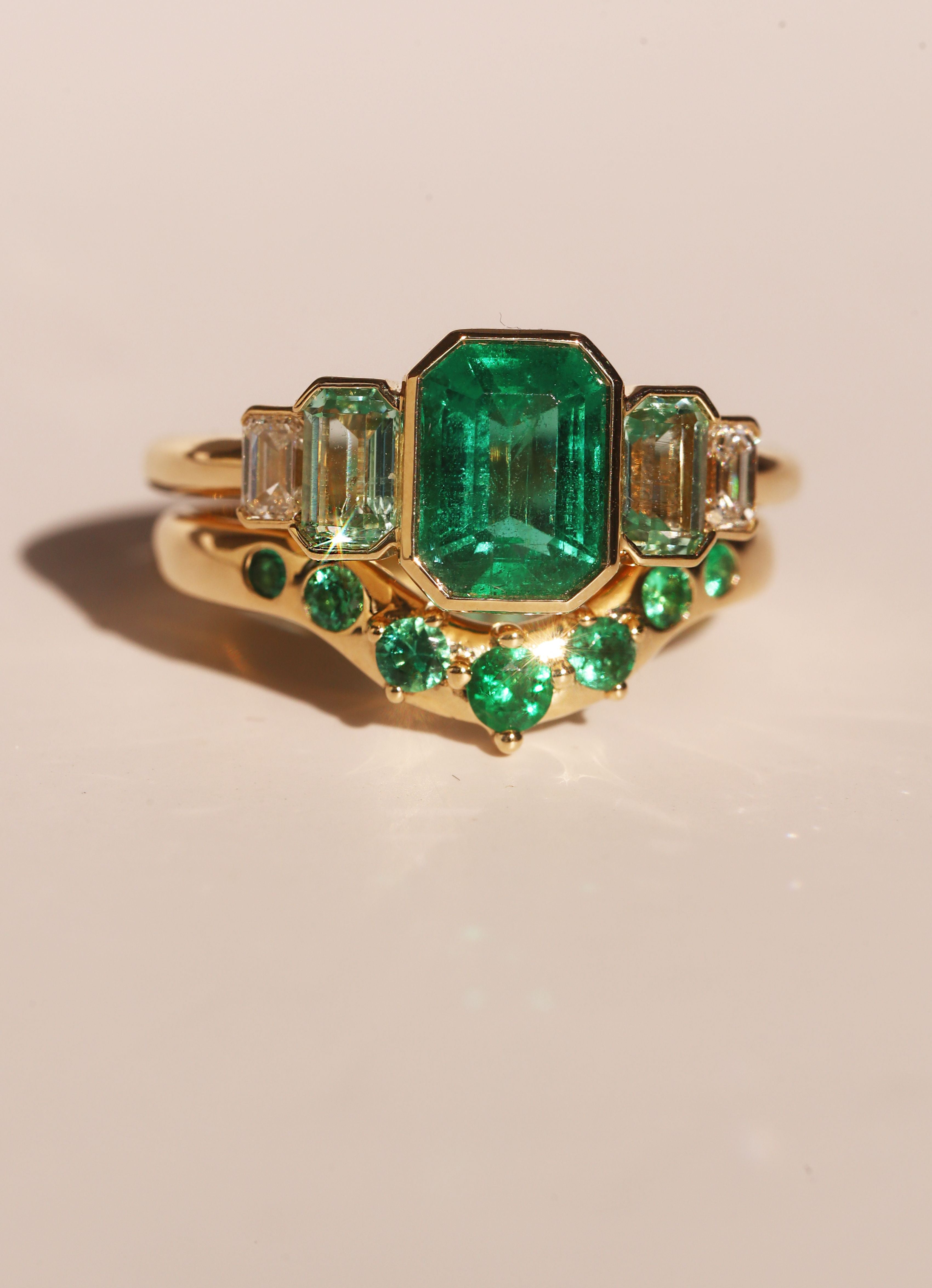 Gold ring with emerald green gemstones on a beige background