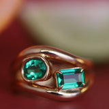 Gold ring with two green gemstones on a blurred background