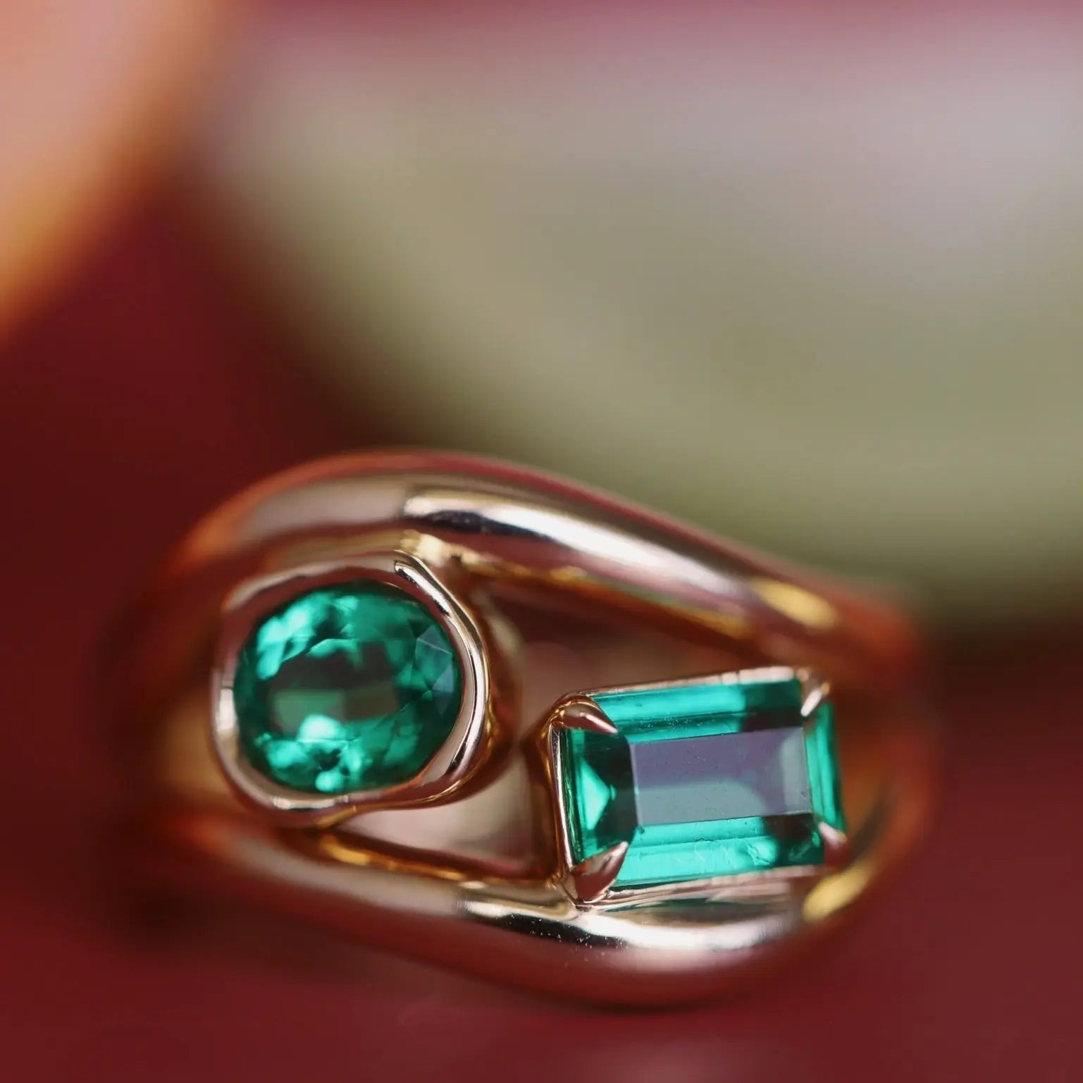 Gold ring with two green gemstones on a blurred background