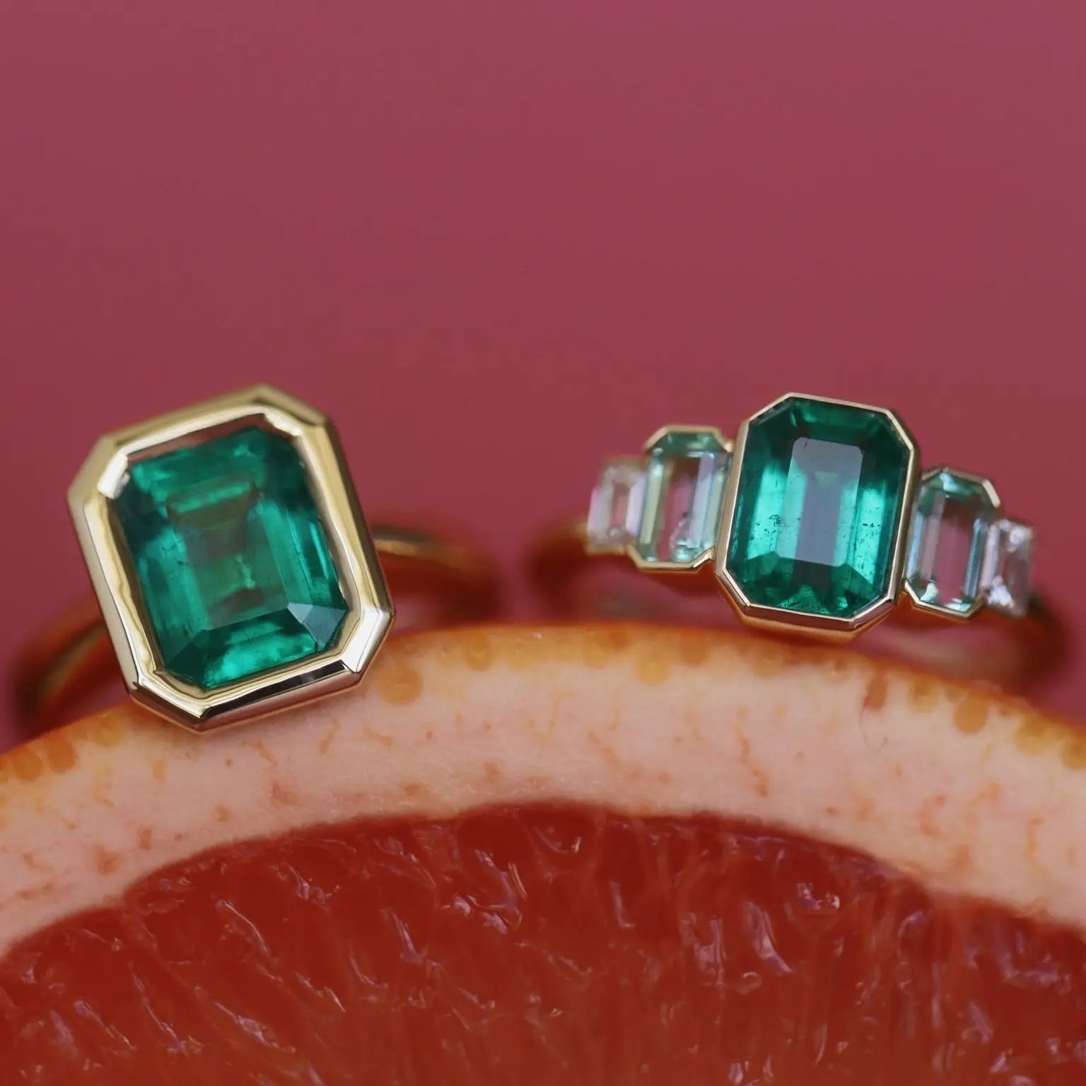 two emerald diamond rings on a grapefruit against a pink background