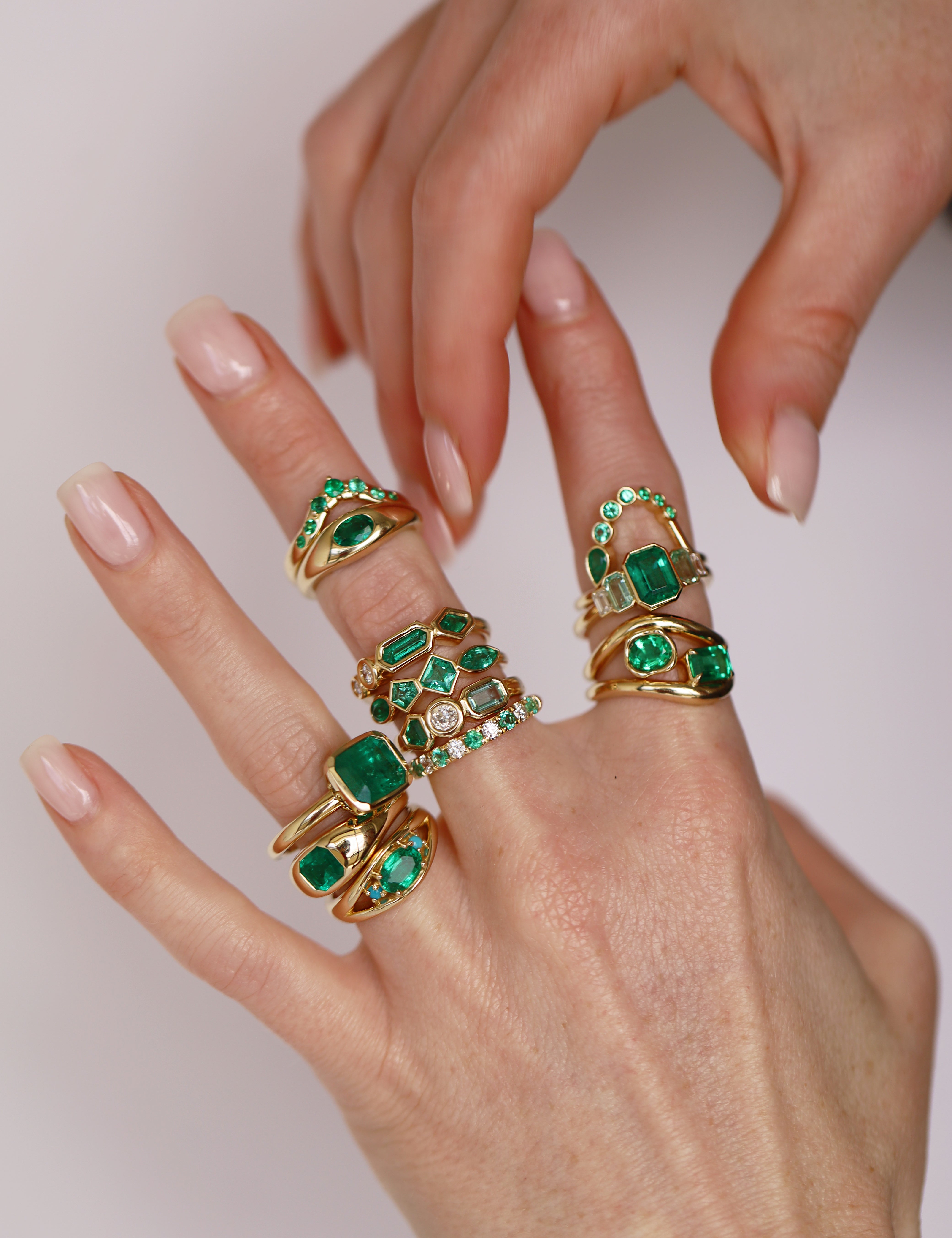 Hands wearing stacked yellow gold rings set with emeralds and diamonds