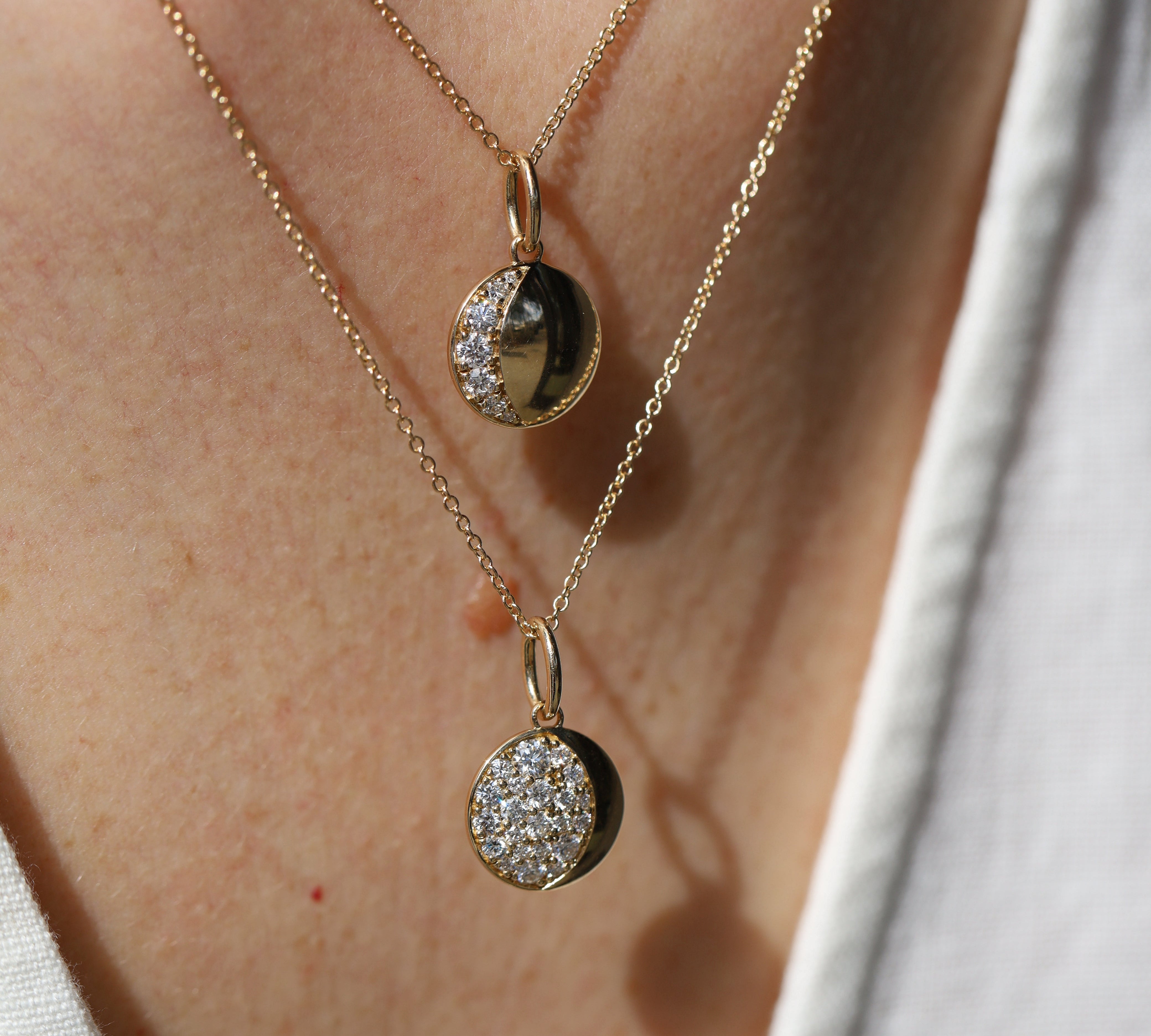 Two gold necklaces with circular pendants on a person's neck.
