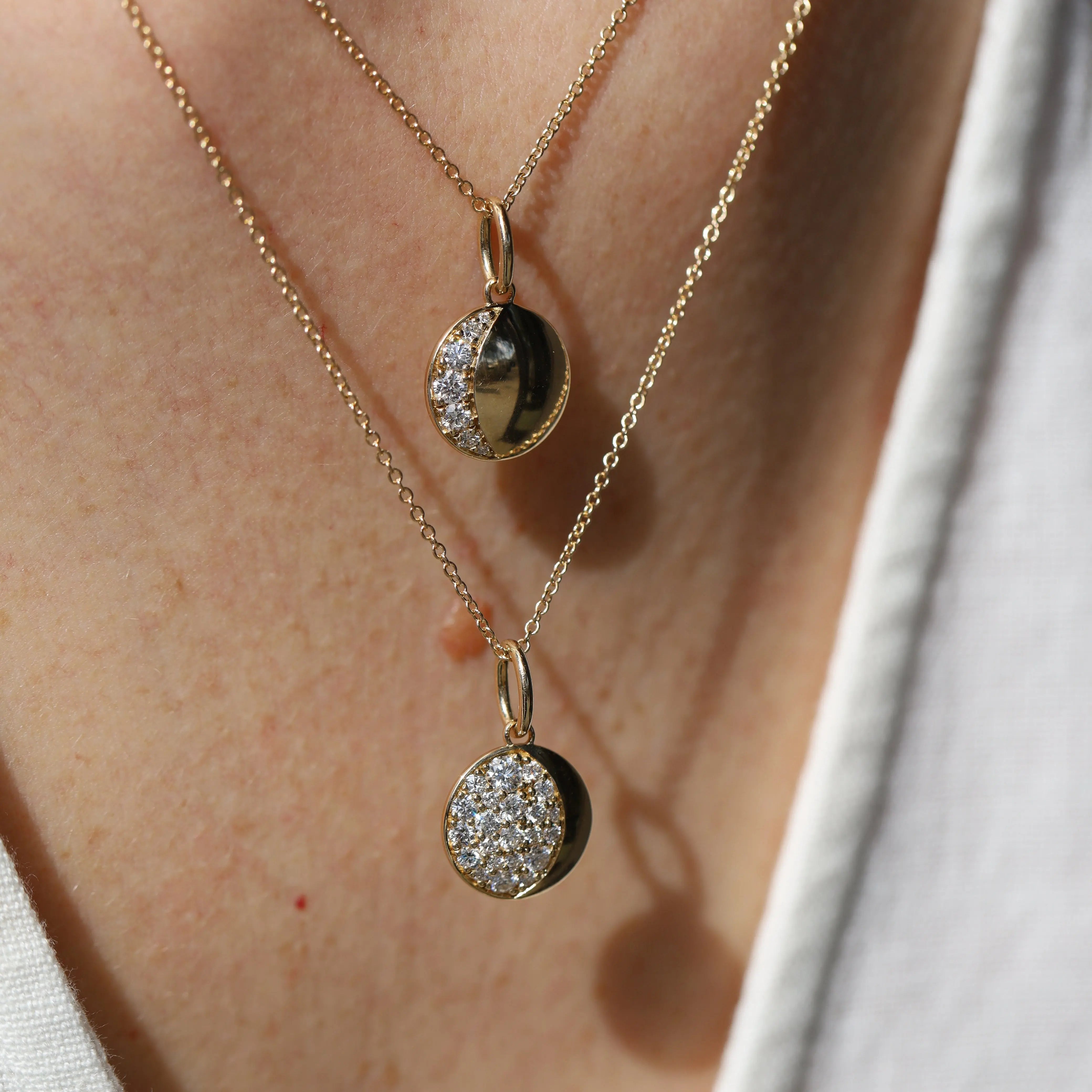 Two gold necklaces with circular pendants on a person's neck.