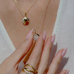 Close-up of a hand wearing gold rings and a gold necklace with a pendant.