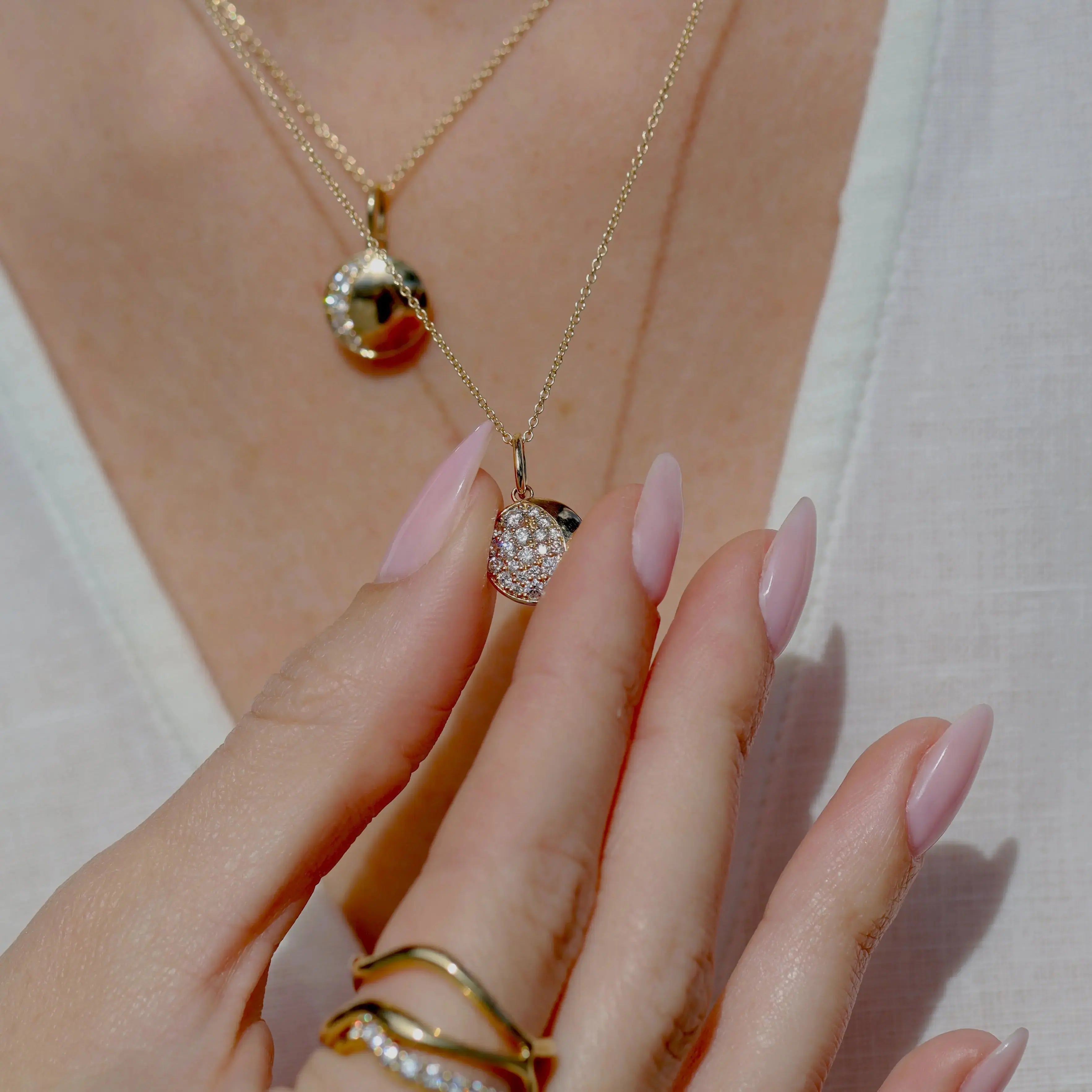 Close-up of a hand wearing gold rings and a gold necklace with a pendant.