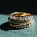 flatlay of three yellow gold and diamodn rings stacked together against a textured green background with shadows