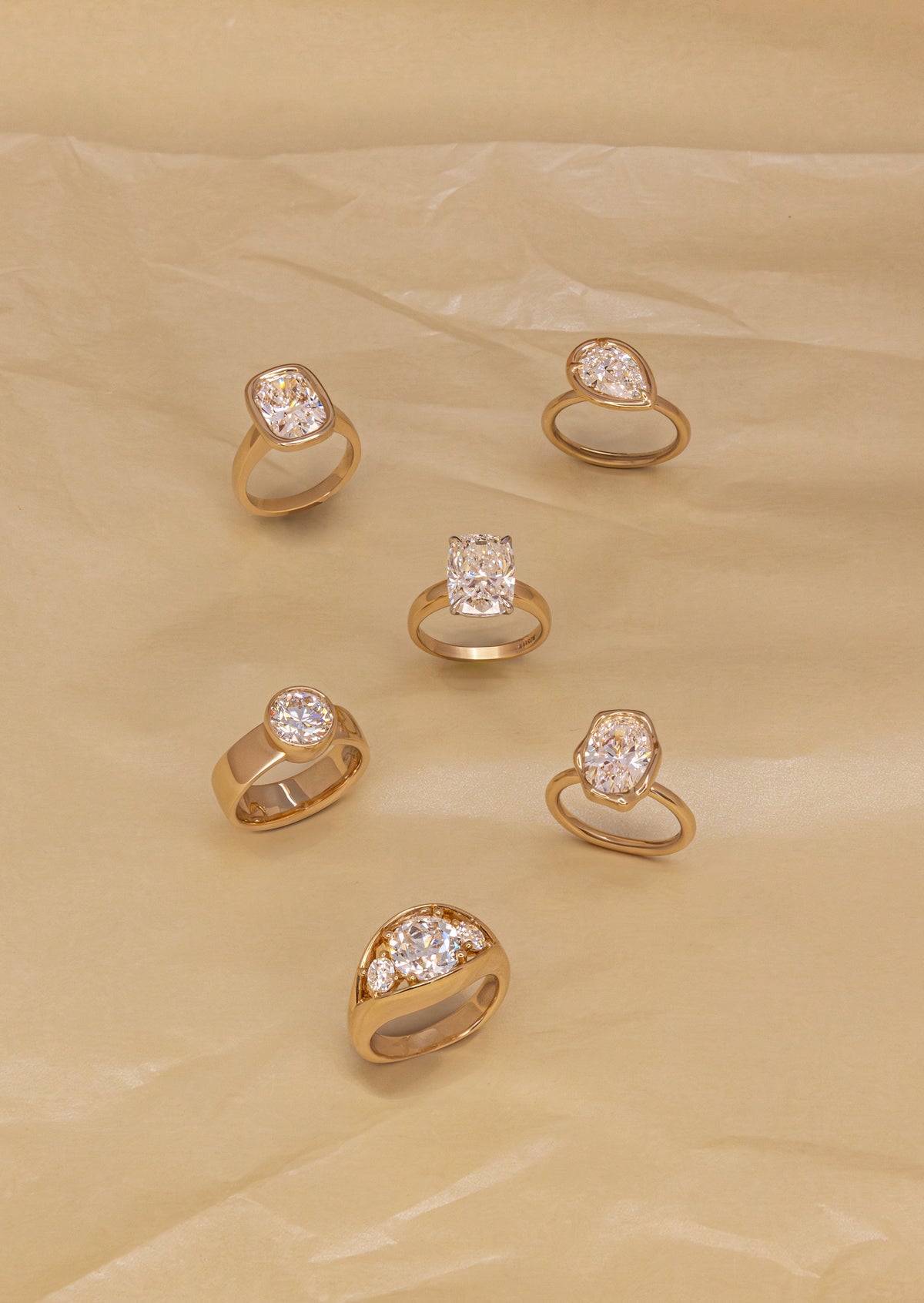 Five yellow gold diamond engagement rings scattered on a pale yellow background