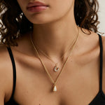 close up of woman's décolletage spotlighting two yellow gold chains of varying weights layered with charms