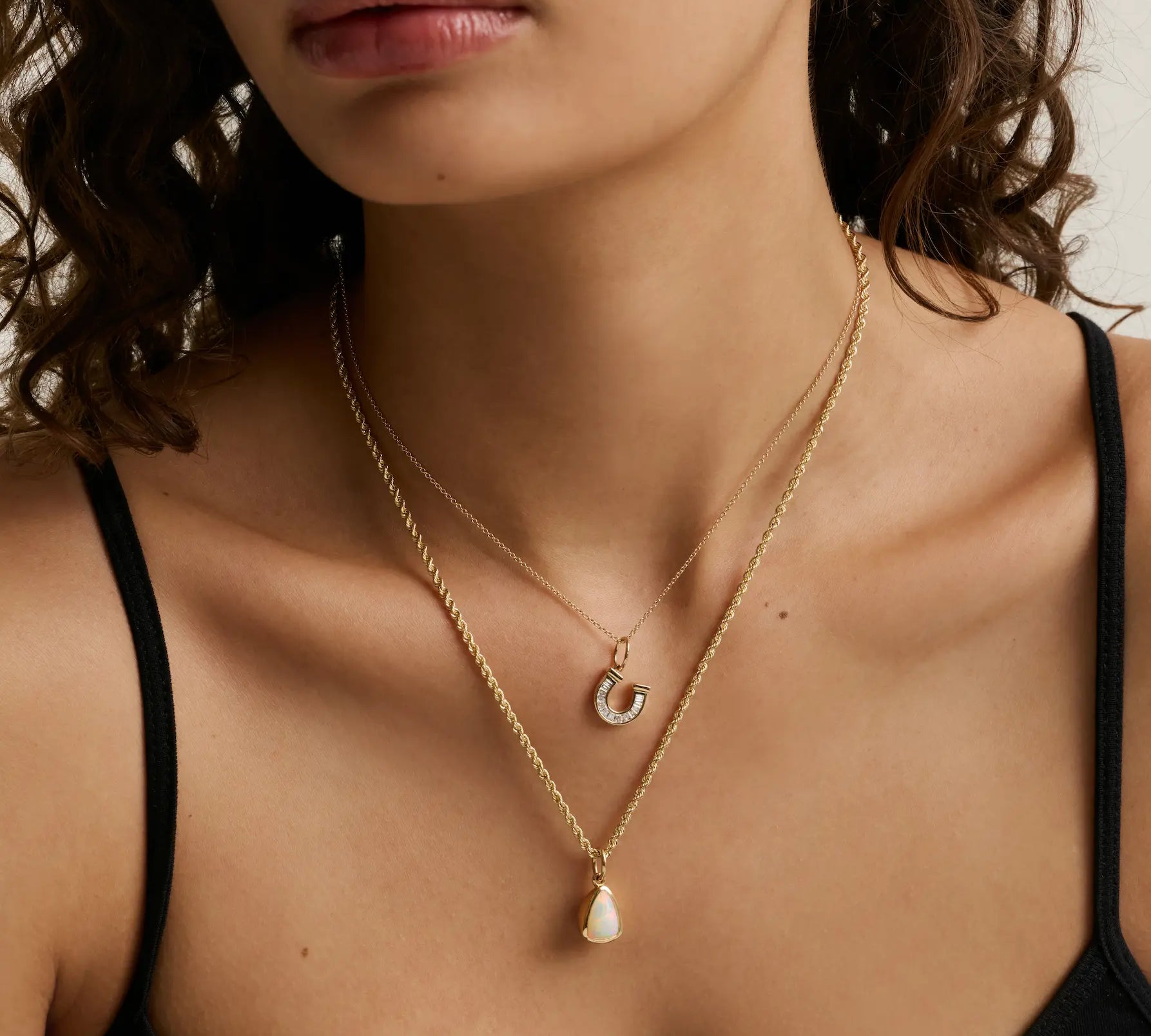 close up of woman's décolletage spotlighting two yellow gold chains of varying weights layered with charms