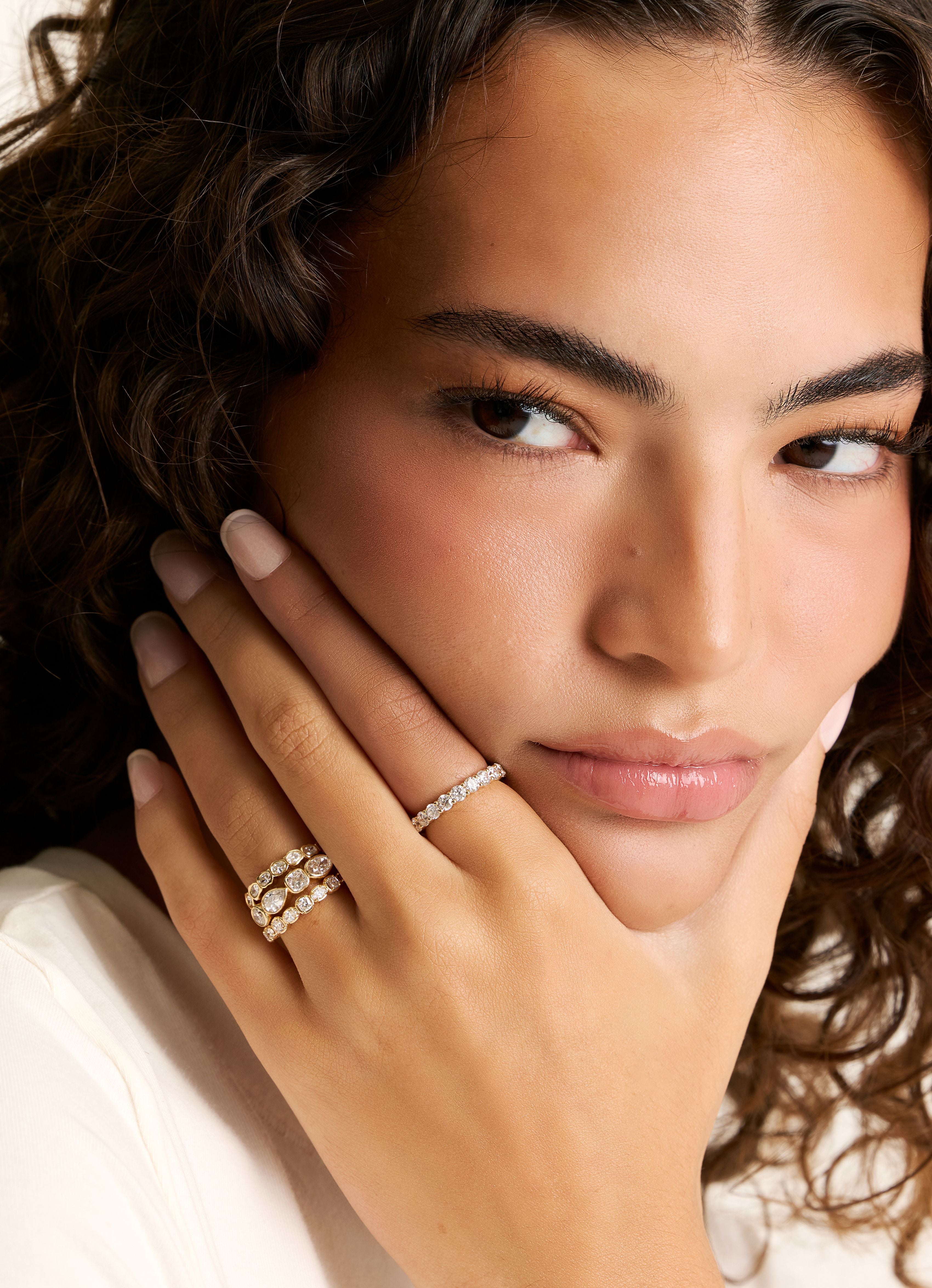 A close-up lifestyle shot of a woman with curly brown hair wearing three delicate diamond rings on her hand.