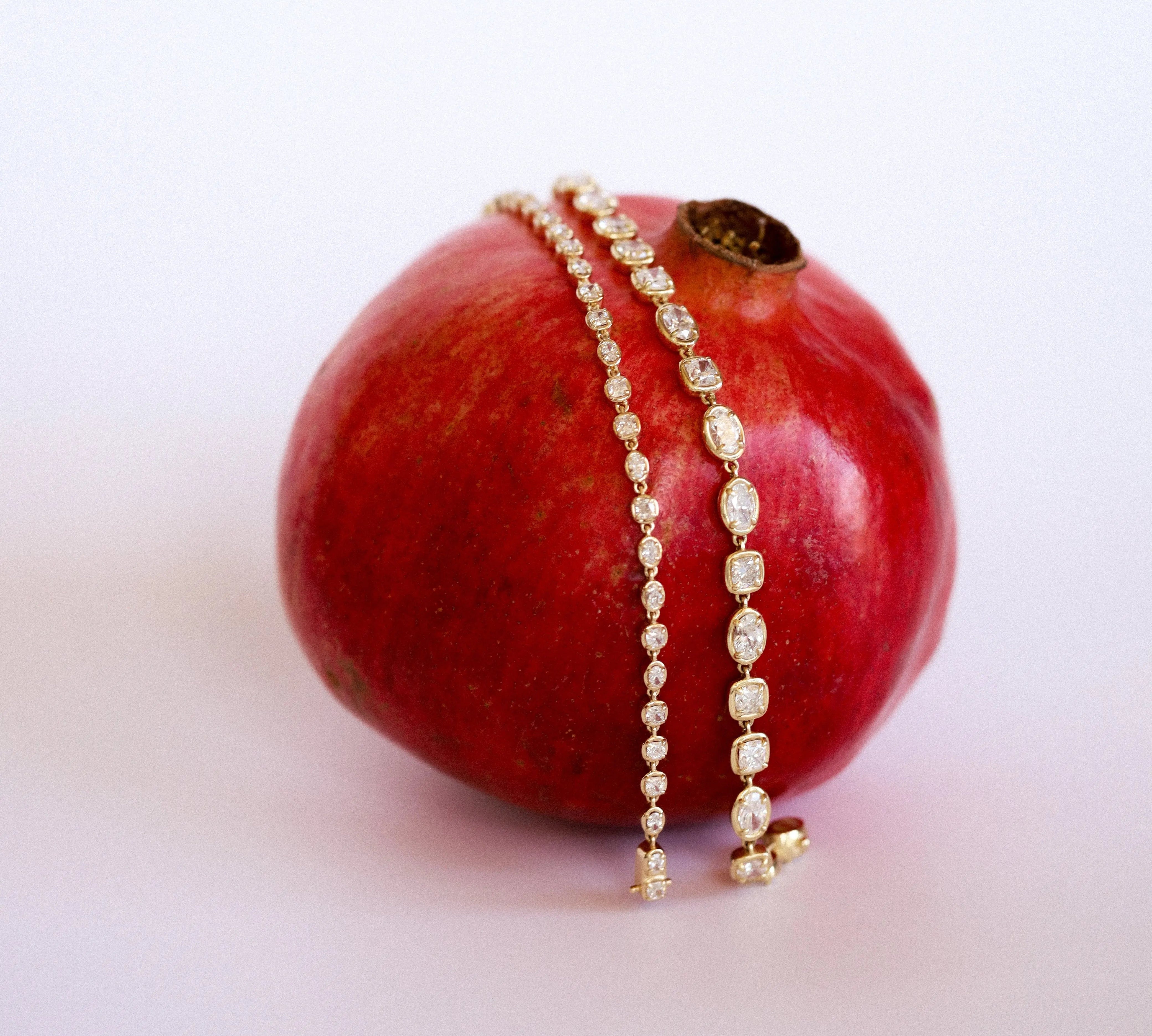 lisse tennis bracelet comparison (regular and mini) both draped over a pomegranate, against a white/pink background