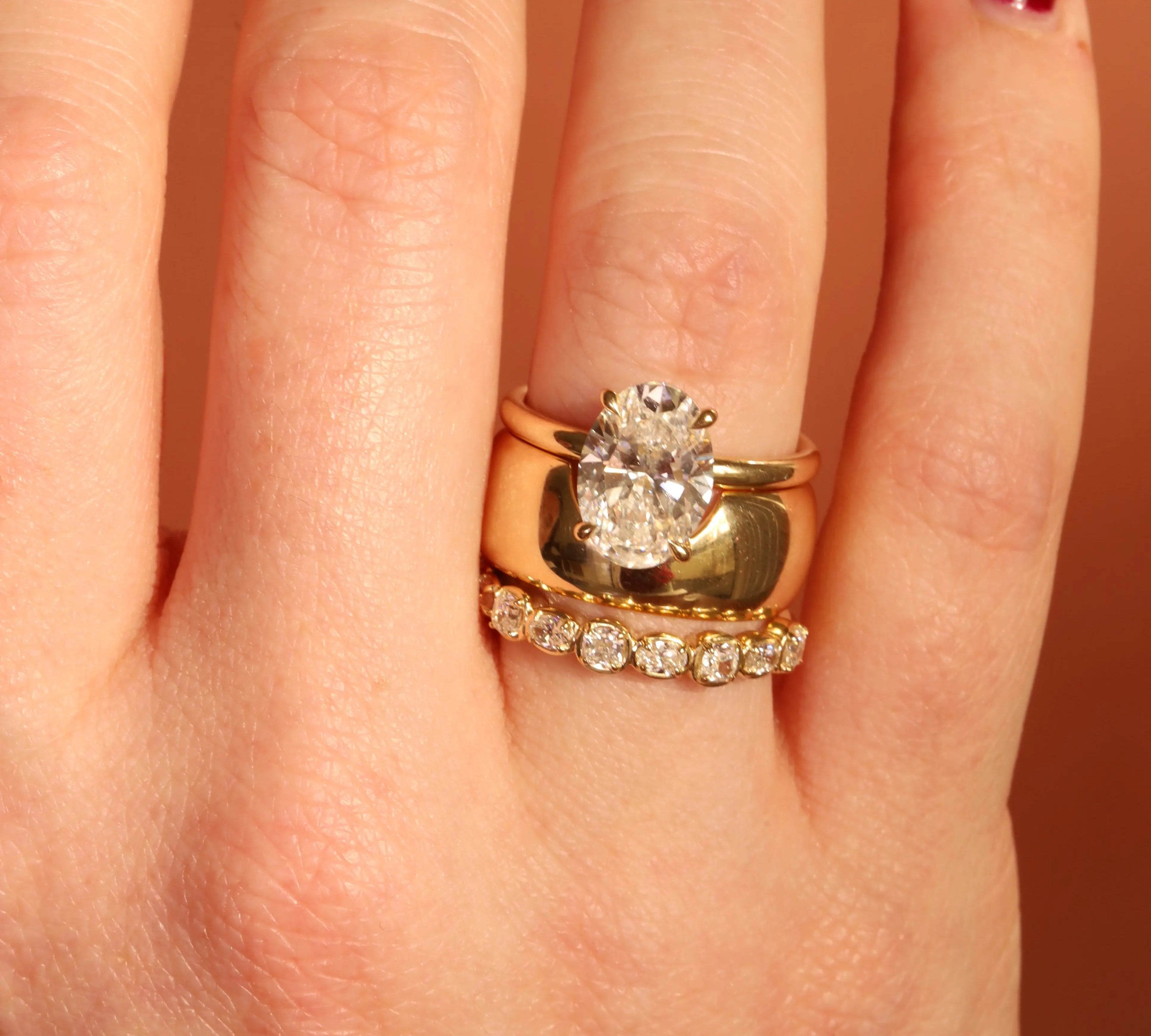 Gold ring with a diamond on a person's finger against a neutral background