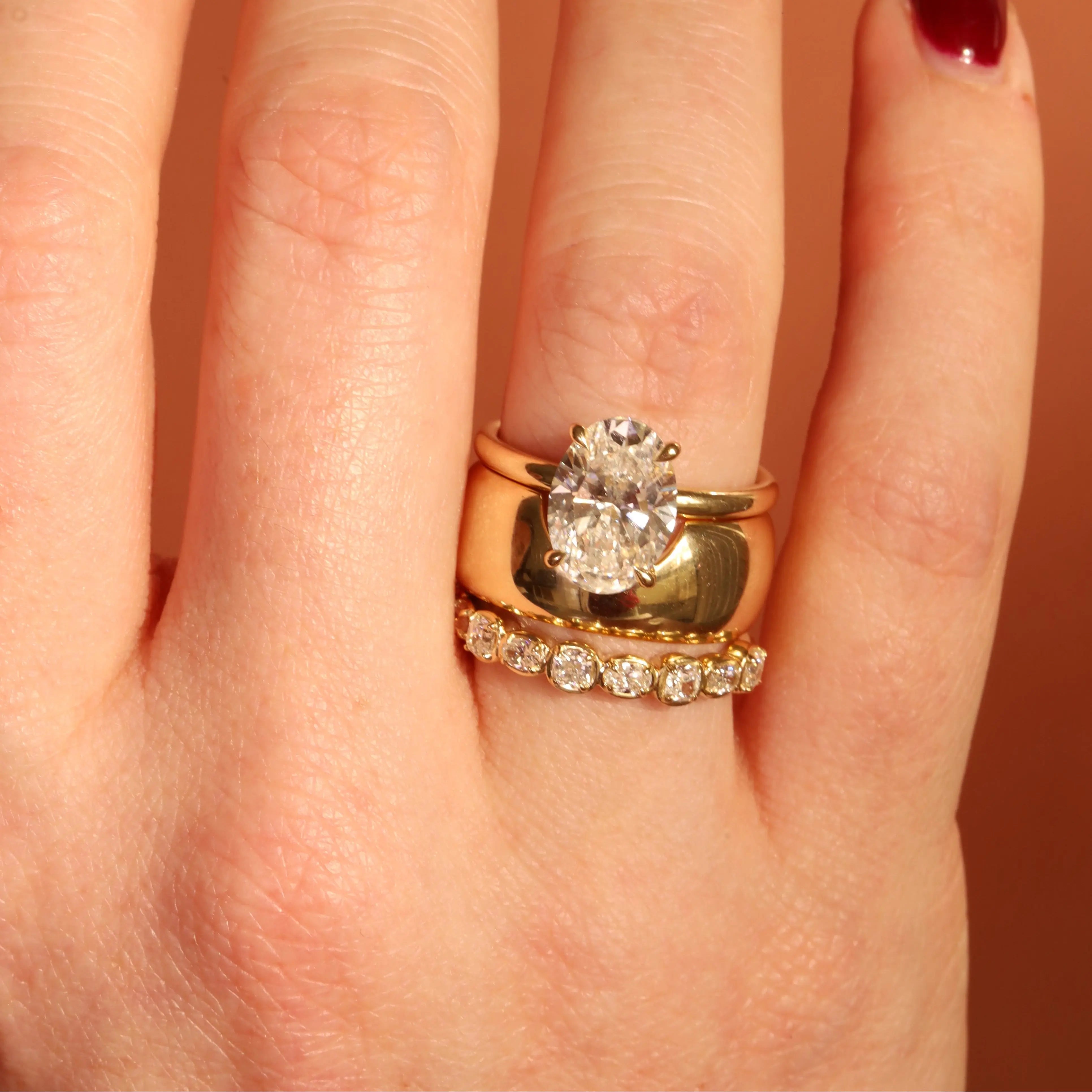 Gold ring with a diamond on a person's finger against a neutral background