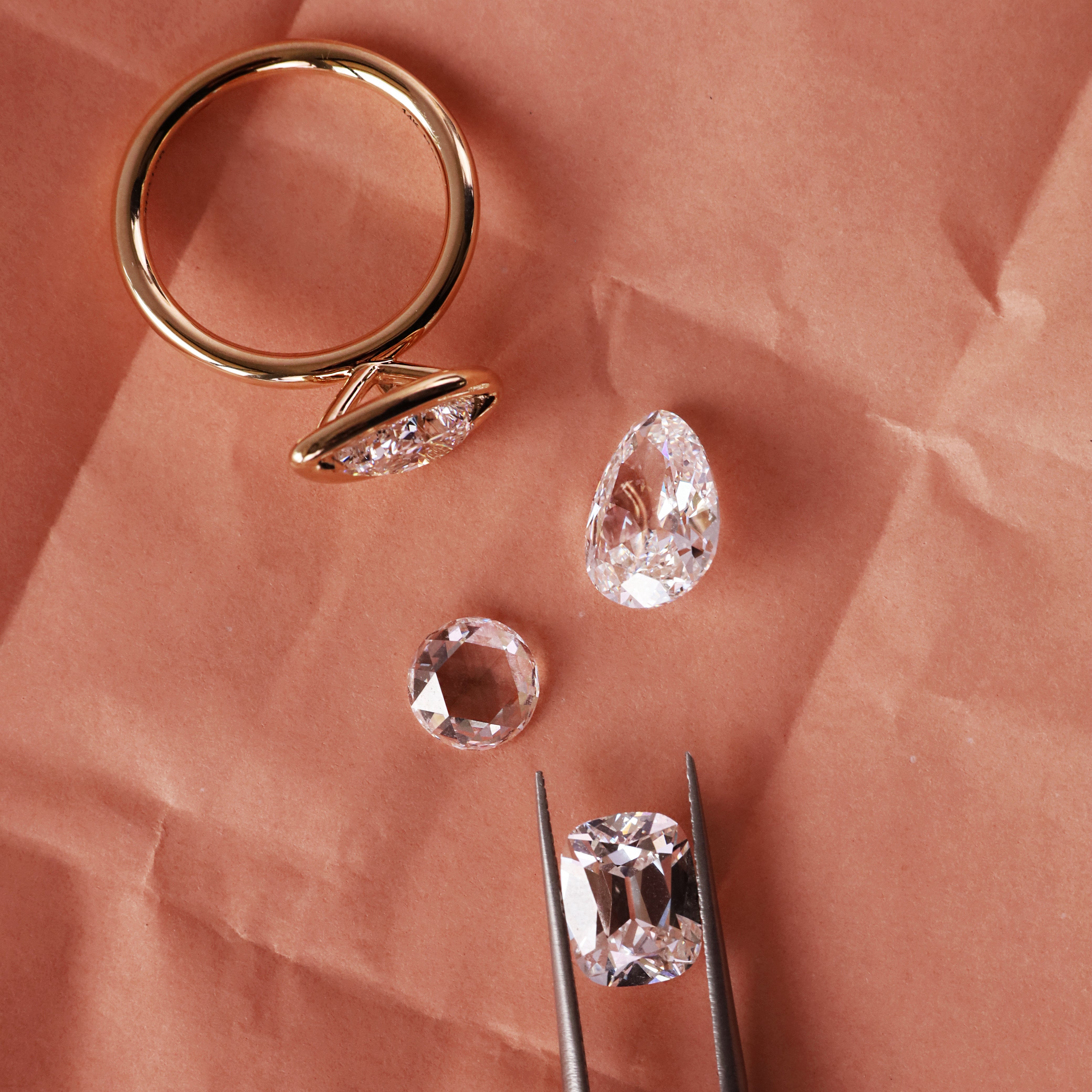 flat lay of gold ring with loose diamonds on a crinkly pink background