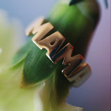 Gold 'MAMA' ring on a green leaf with a blurred background