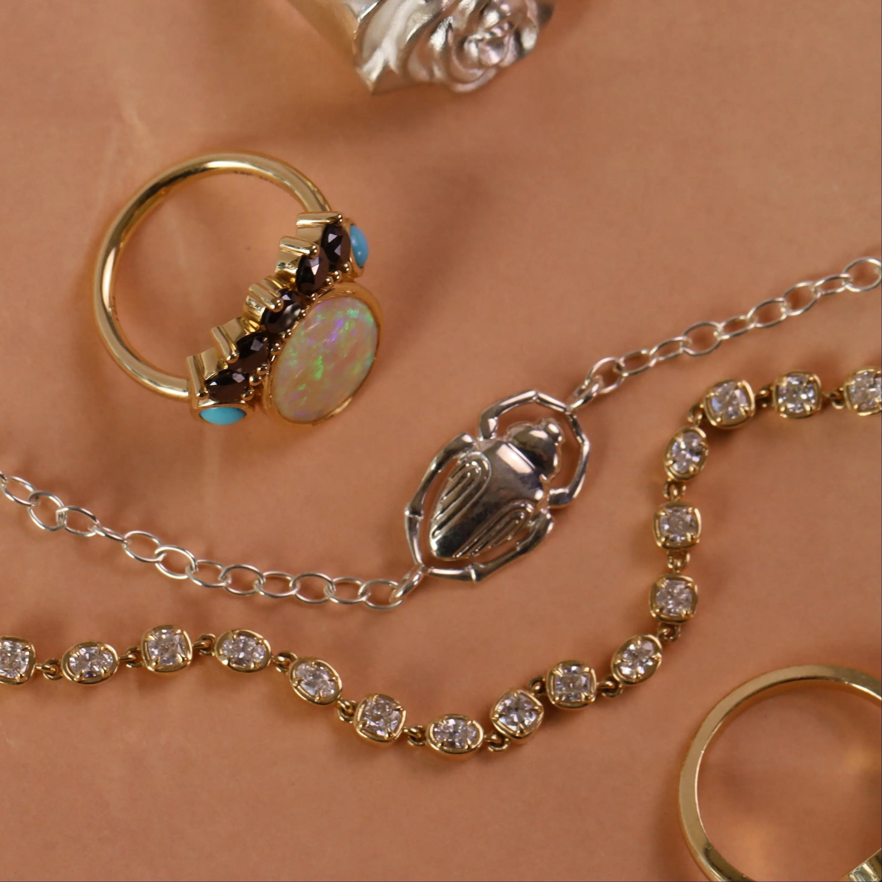 Flat lay of various pieces of jewelry on an orange background, featuring an opal ring, a silver scarab bracelet, and a tennis bracelet