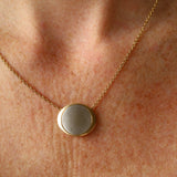 Gold necklace with a round pendant on a person's neck