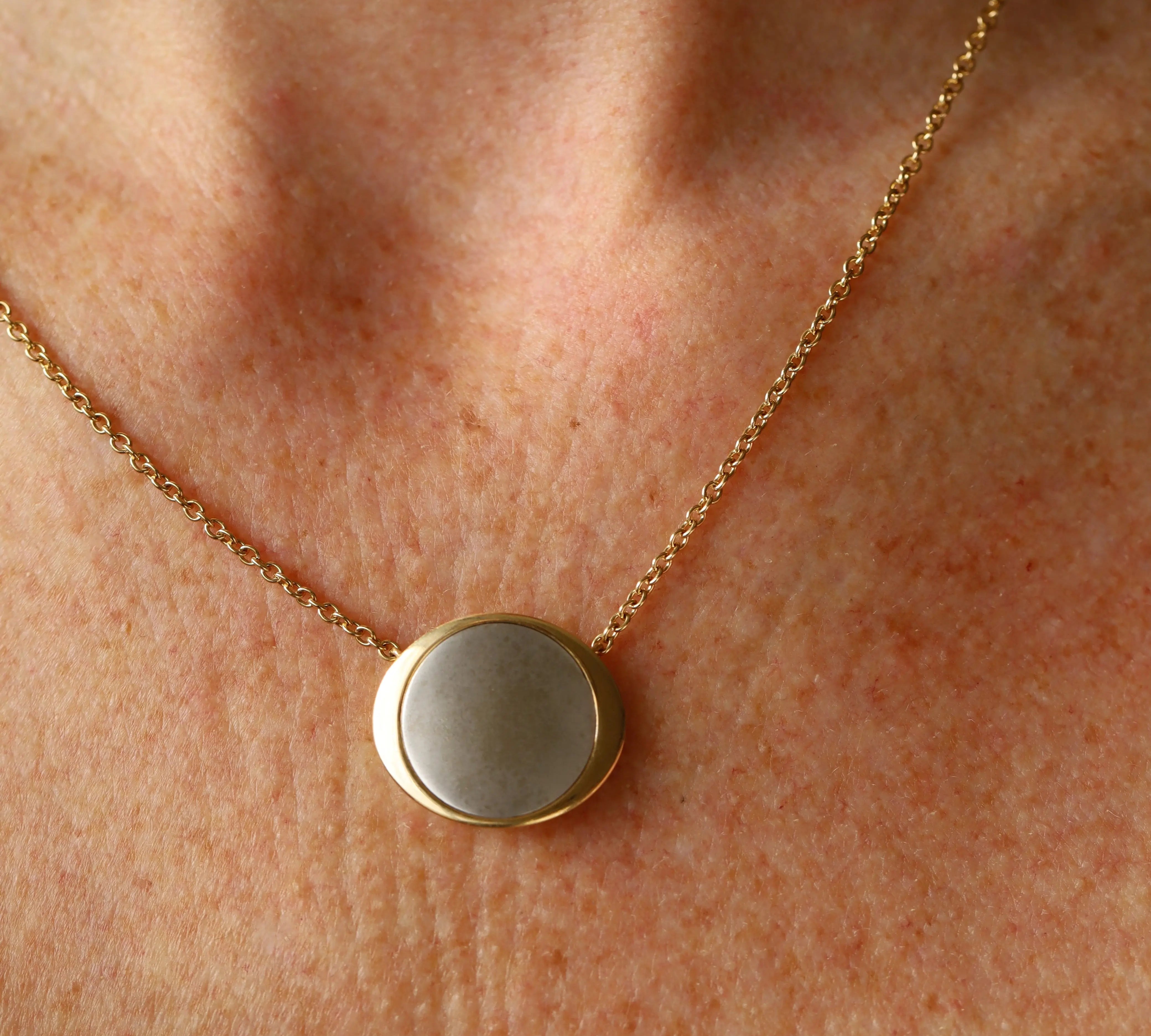 Gold necklace with a round pendant on a person's neck