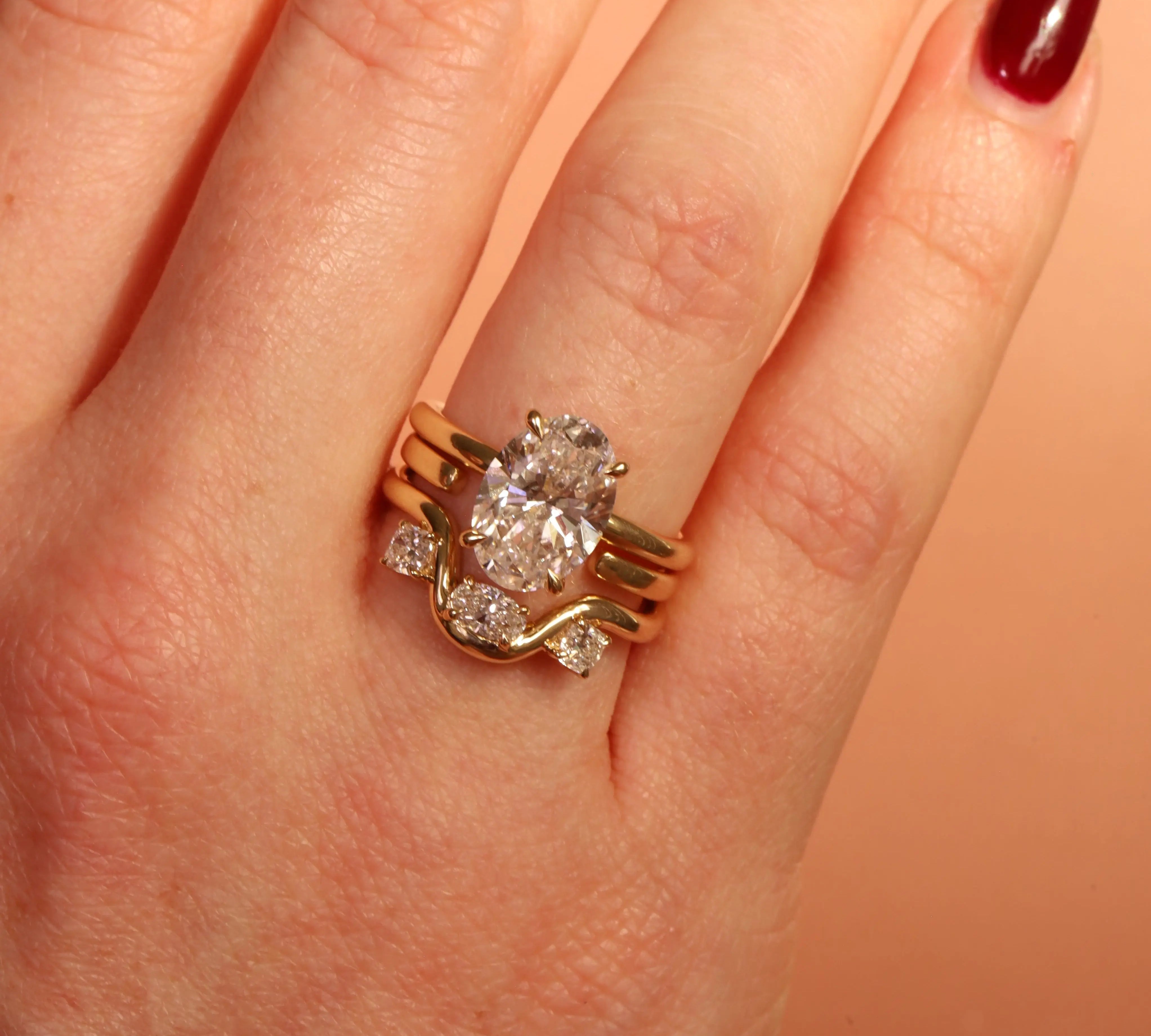 Gold ring with a diamond on a hand against a peach background