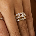 Close-up of a hand wearing three gold eternity rings set with clear round and pear-cut diamonds, with a fourth ring partially visible on the adjacent finger.