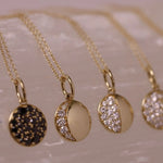 Gold necklaces with various pendants on a textured surface