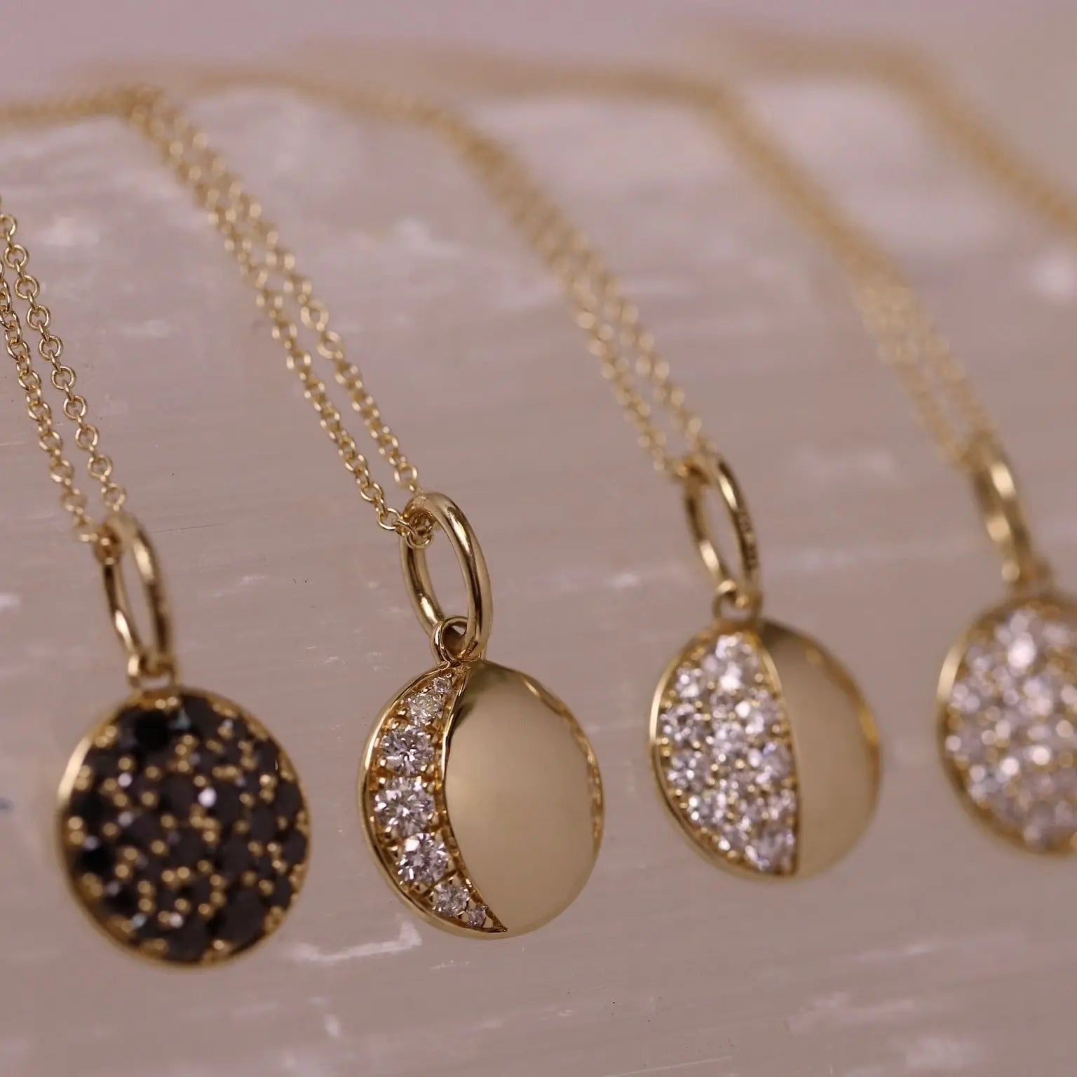 Gold necklaces with various pendants on a textured surface