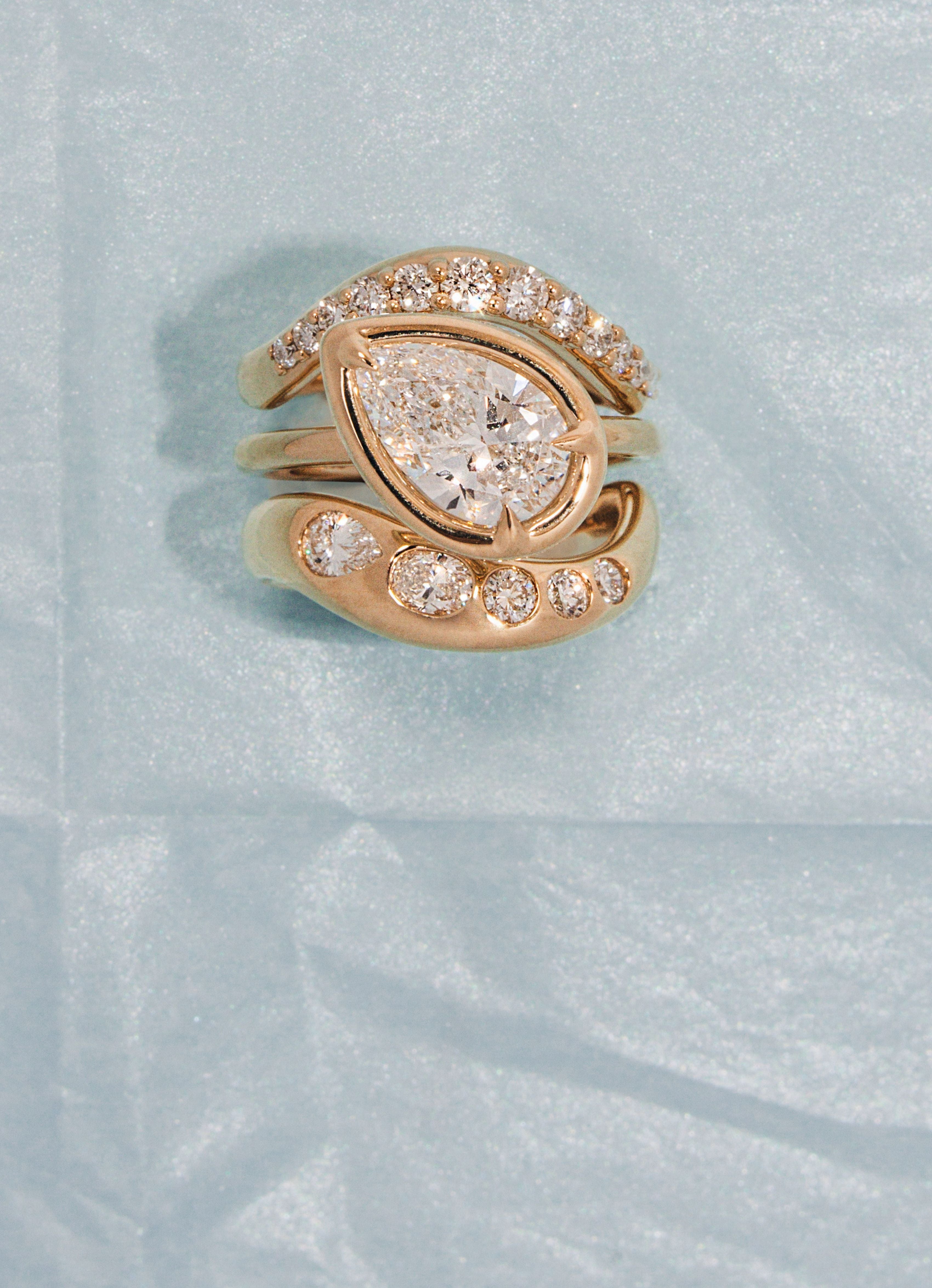Gold ring with a pear-shaped center stone and smaller diamonds on a light blue background