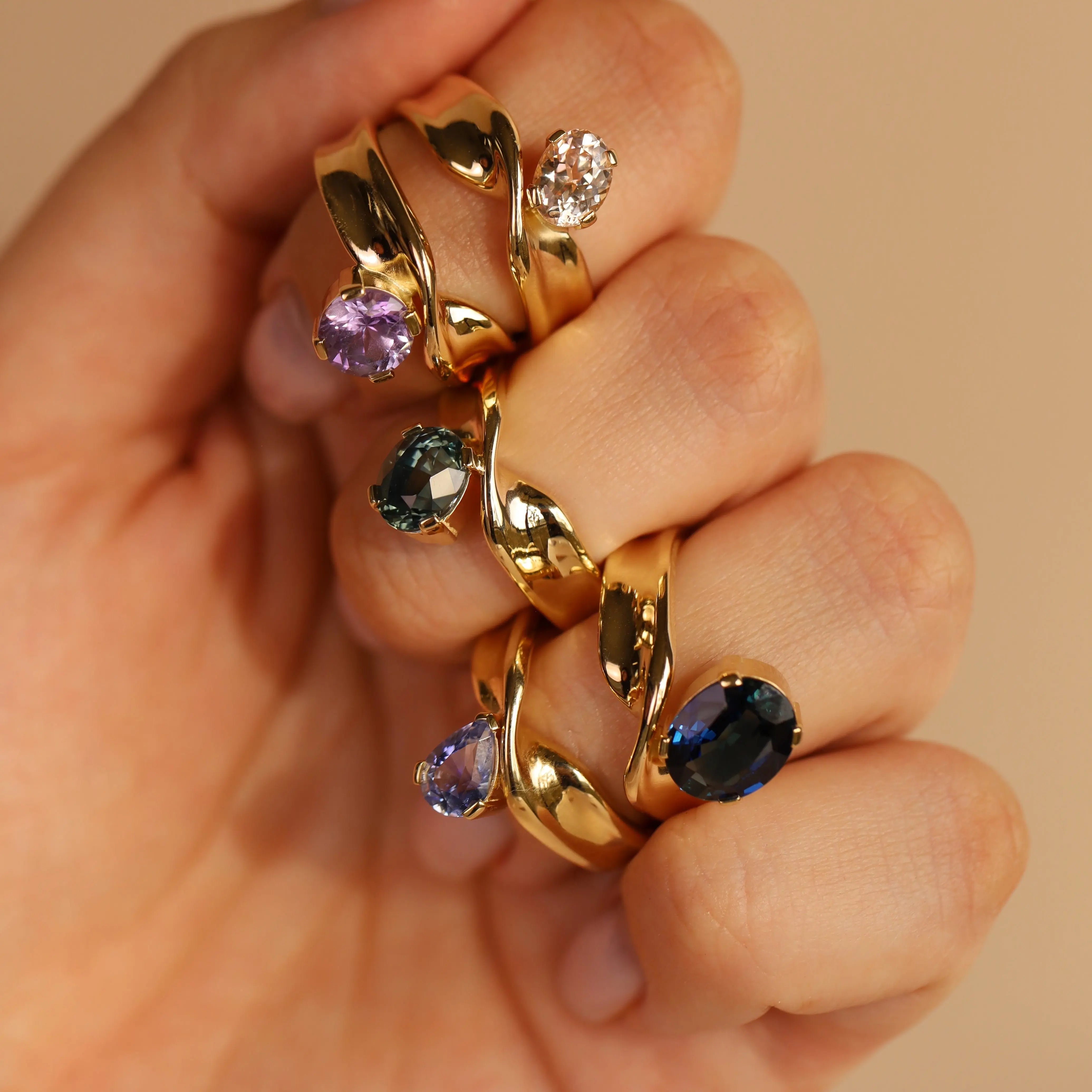 Gold rings with gemstones on a hand against a beige background