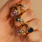 Gold rings with gemstones on a hand against a beige background